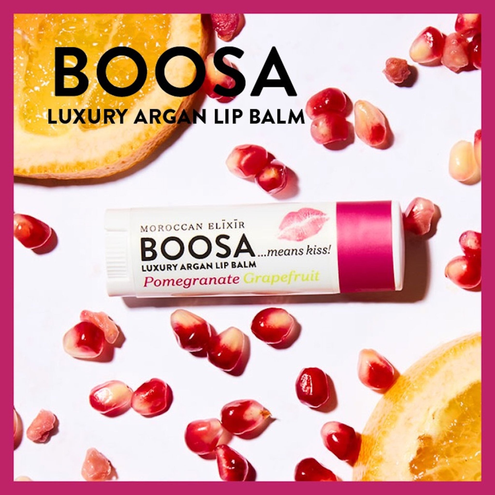 Lip balm tube with BOOSA brand text, white and pink packaging, surrounded by pomegranate seeds