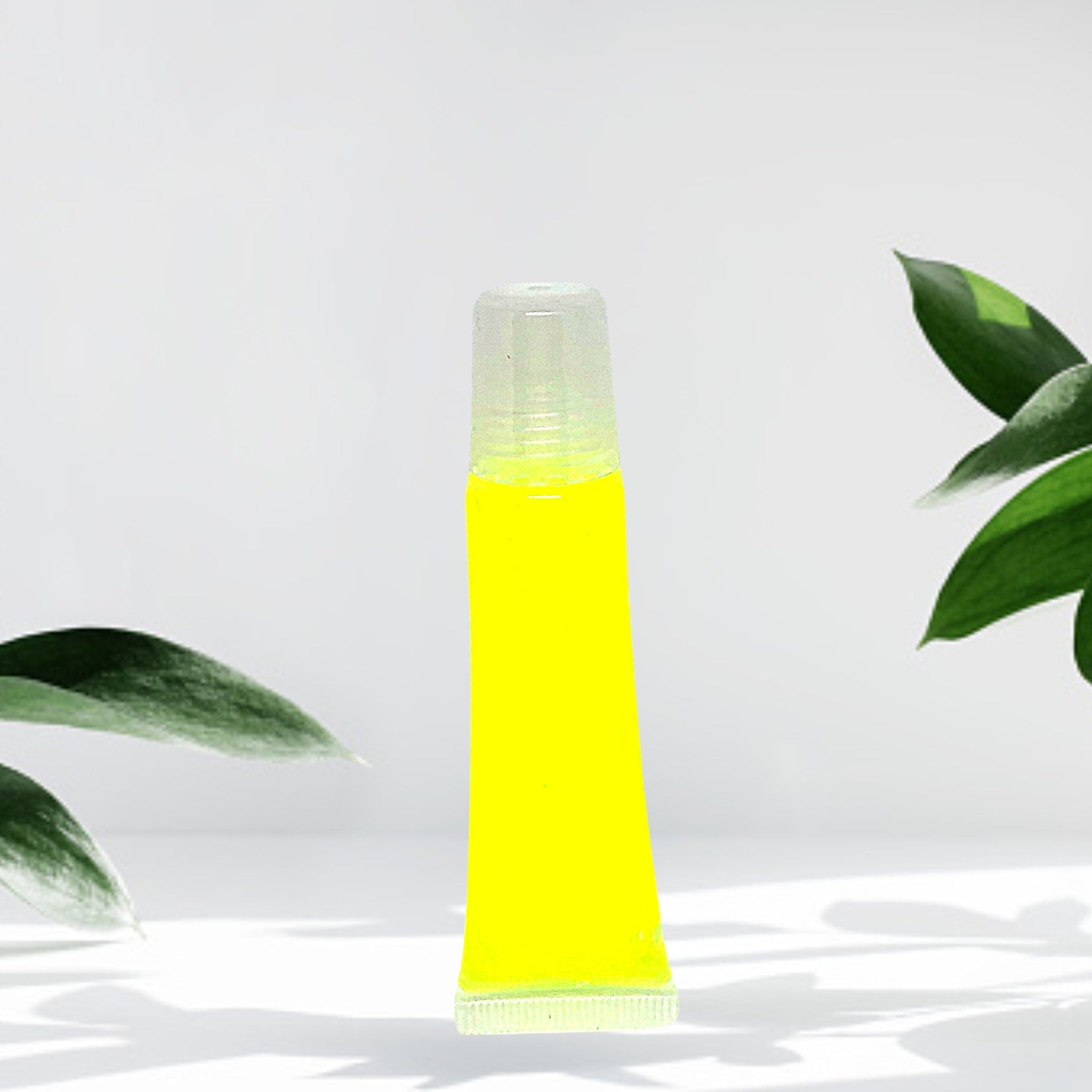Lip gloss tube, yellow liquid, clear plastic tube, green leaves in background