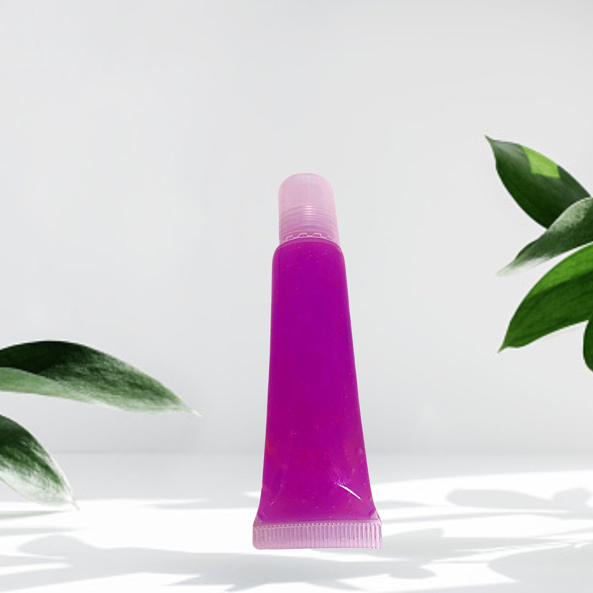 Lip gloss tube with purple gloss, clear plastic tube, and pink cap, shown in studio setting