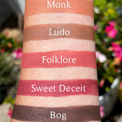 Lipstick swatches in various colors on skin, with text labels "Monk", "Ludo", "Folklore", "Sweet Deceit", and "Bog