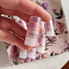 Lip balm, pink tinted tube, clear plastic, held in hand with other balms