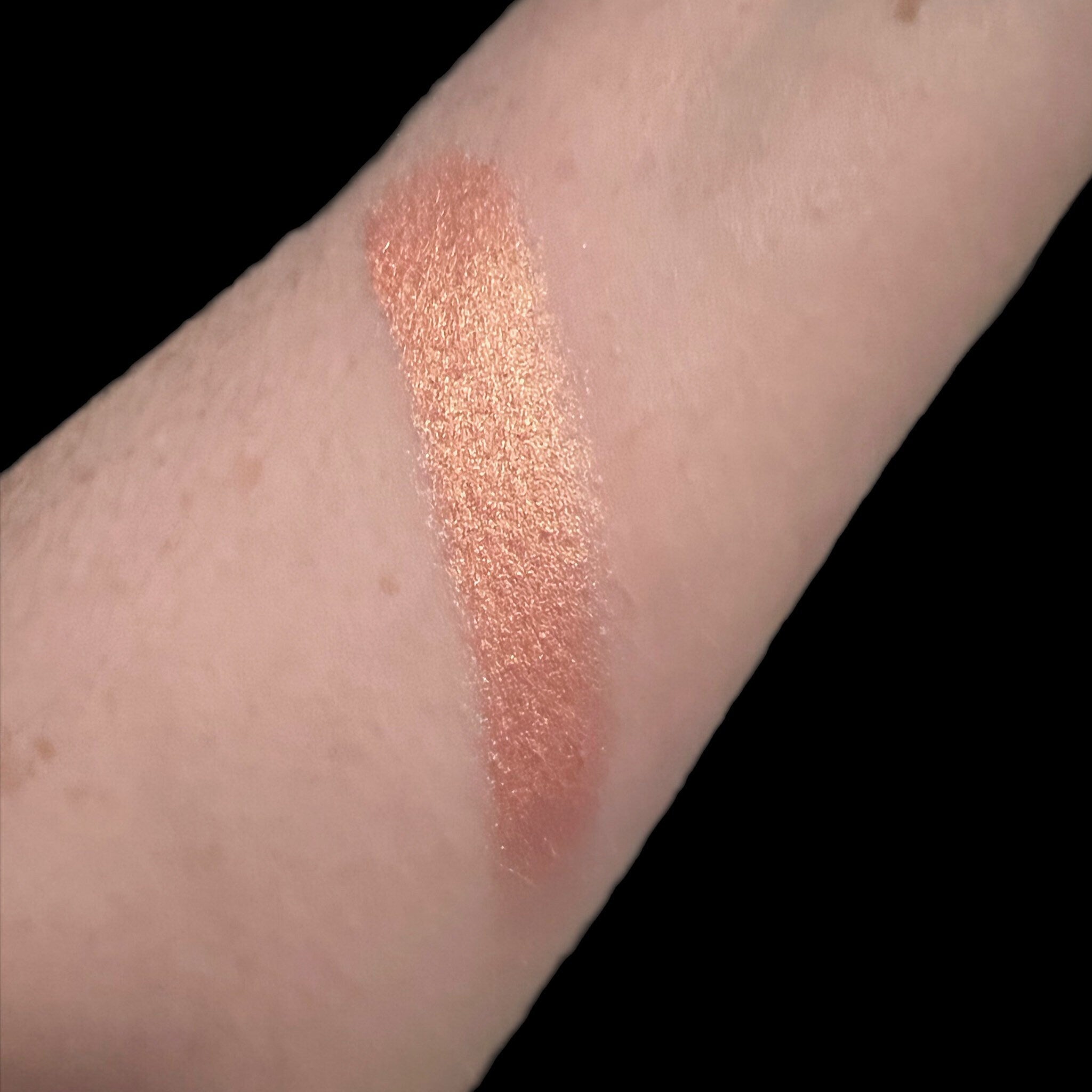 Hand applying peach-toned vegan eyeshadow with a fluffy brush for a soft blended look on the eyelid.