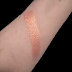 Hand applying peach-toned vegan eyeshadow with a fluffy brush for a soft blended look on the eyelid.