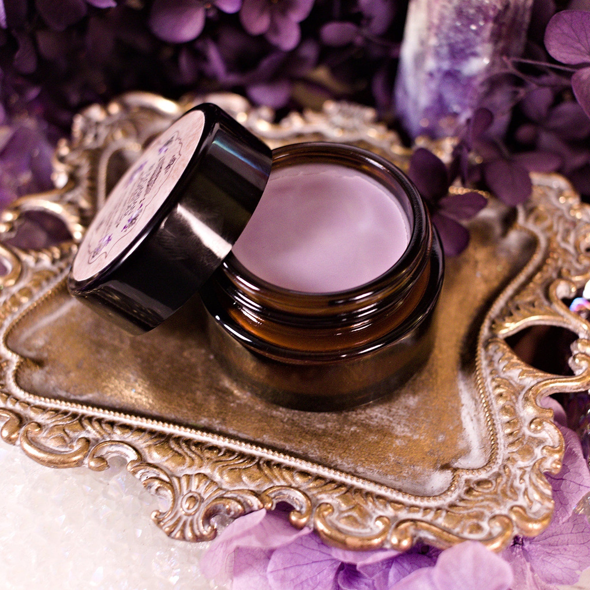 Cosmetic jar with black lid, brown glass, and light purple cream on ornate gold tray