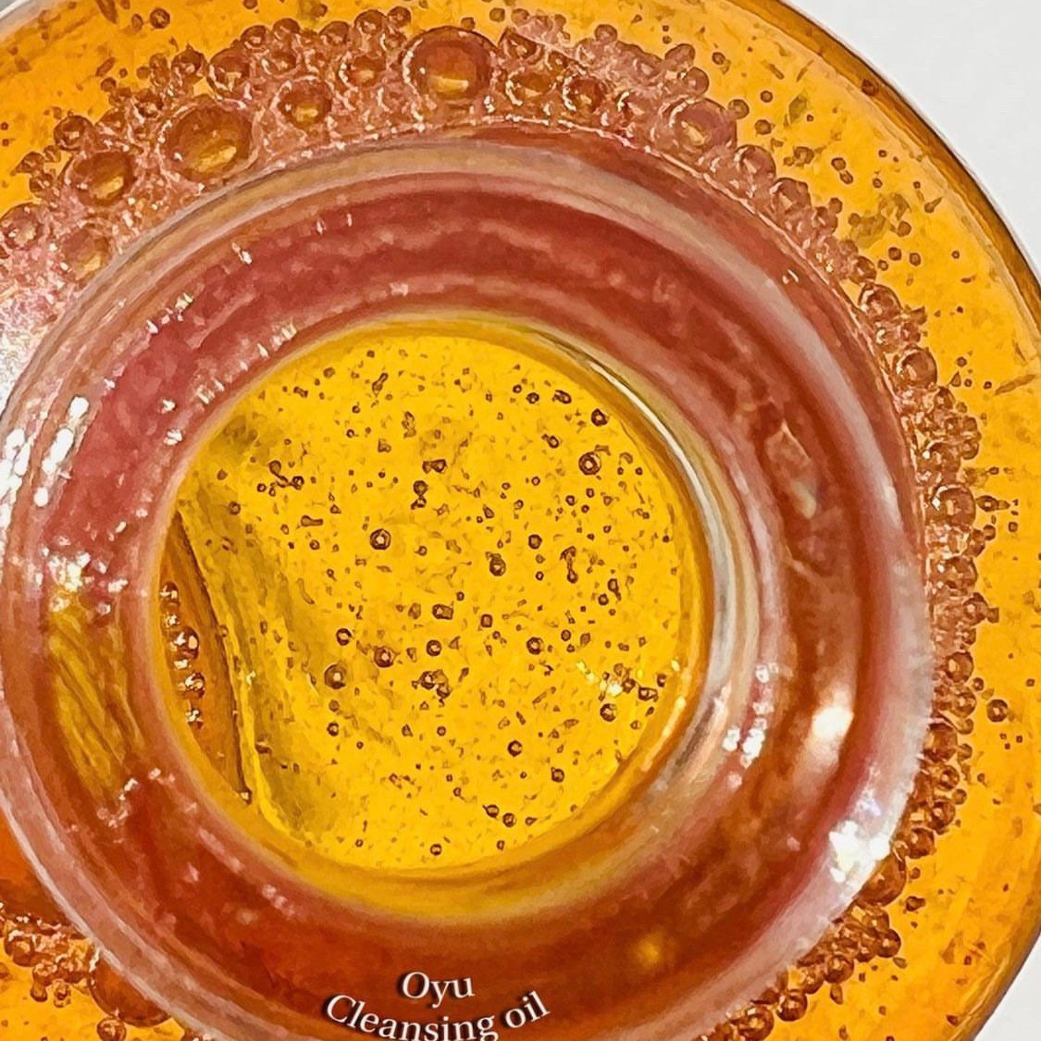 Cleansing oil close-up, yellow and orange liquid with bubbles, Oyu brand visible