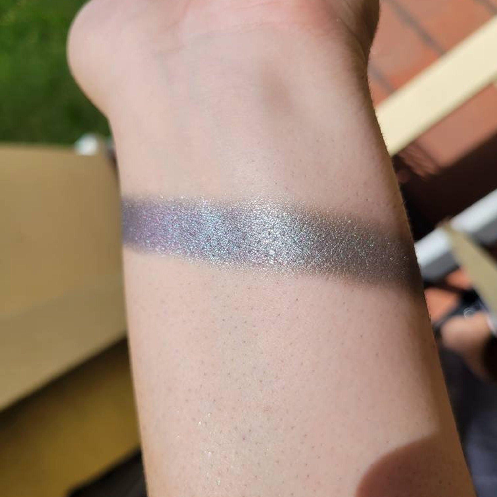 Eyeshadow swatch with iridescent shimmer, silver and purple tones, applied on skin