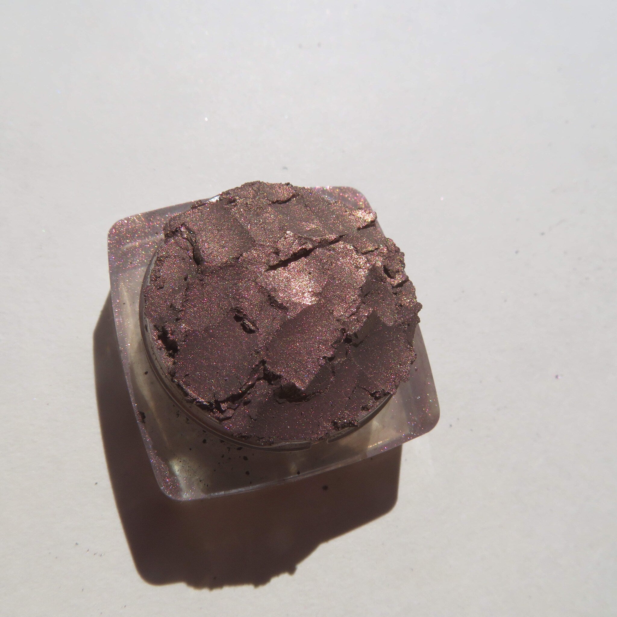 Close-up of loose mineral eyeshadow in dark brown with shimmering rose metal flecks, vegan and talc-free