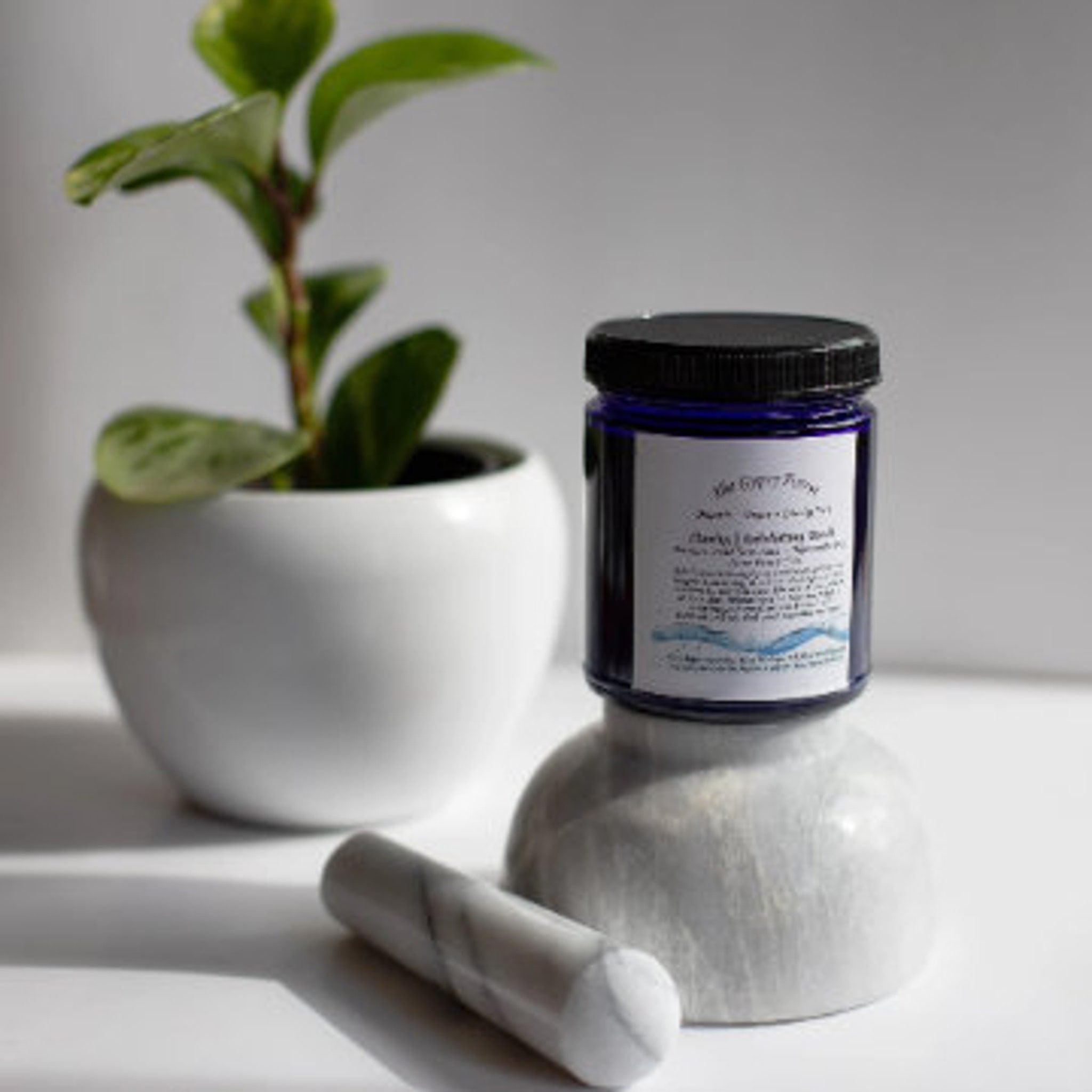 Blue glass jar with black lid, white label, and marble mortar and pestle set on white surface