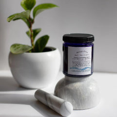 Blue glass jar with black lid, white label, and marble mortar and pestle set on white surface