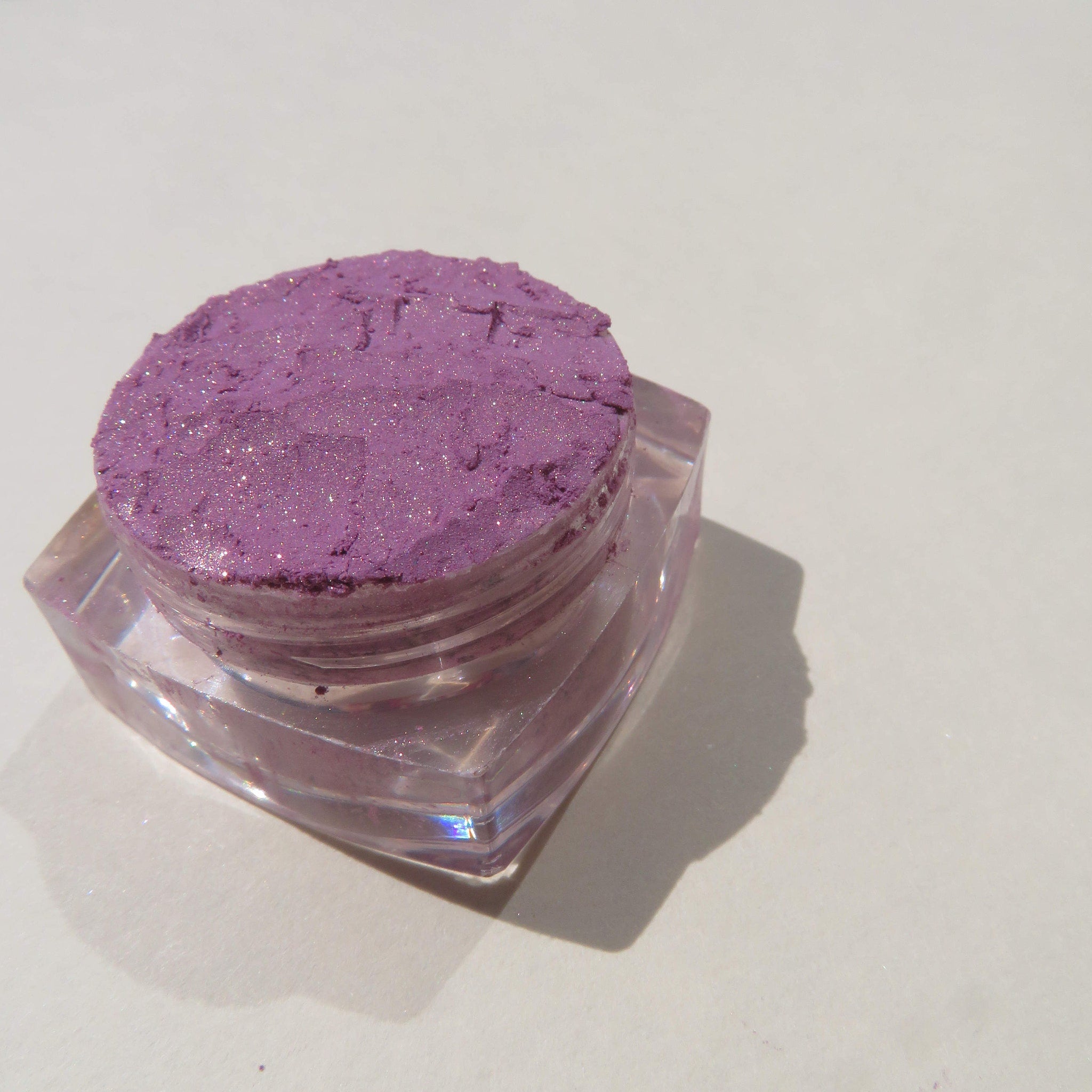 Close-up of Jessica Pure Mineral Eyeshadow loose pigment in shimmering purple, showcasing fine sparkle texture