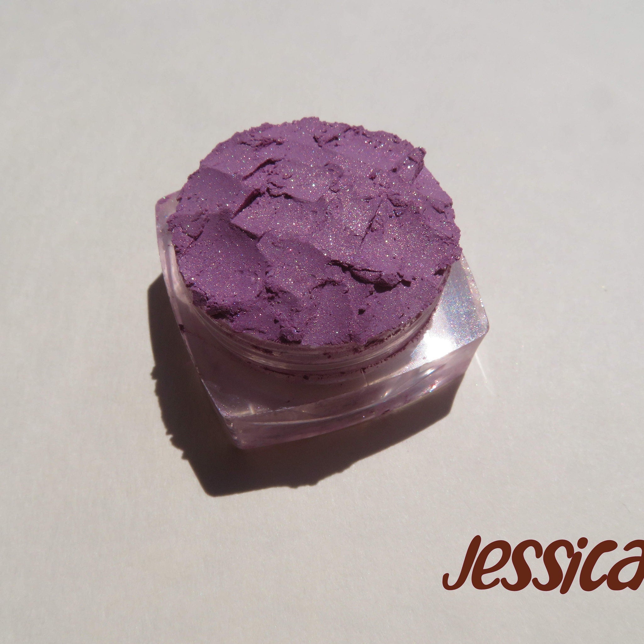 Side view of Jessica Pure Mineral Eyeshadow in purple shimmer loose pigment, showcasing fine sparkle texture in jar