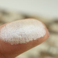 Woman applying shimmering vegan cream eyeshadow with fingertip to eyelid, showcasing smooth blendable texture