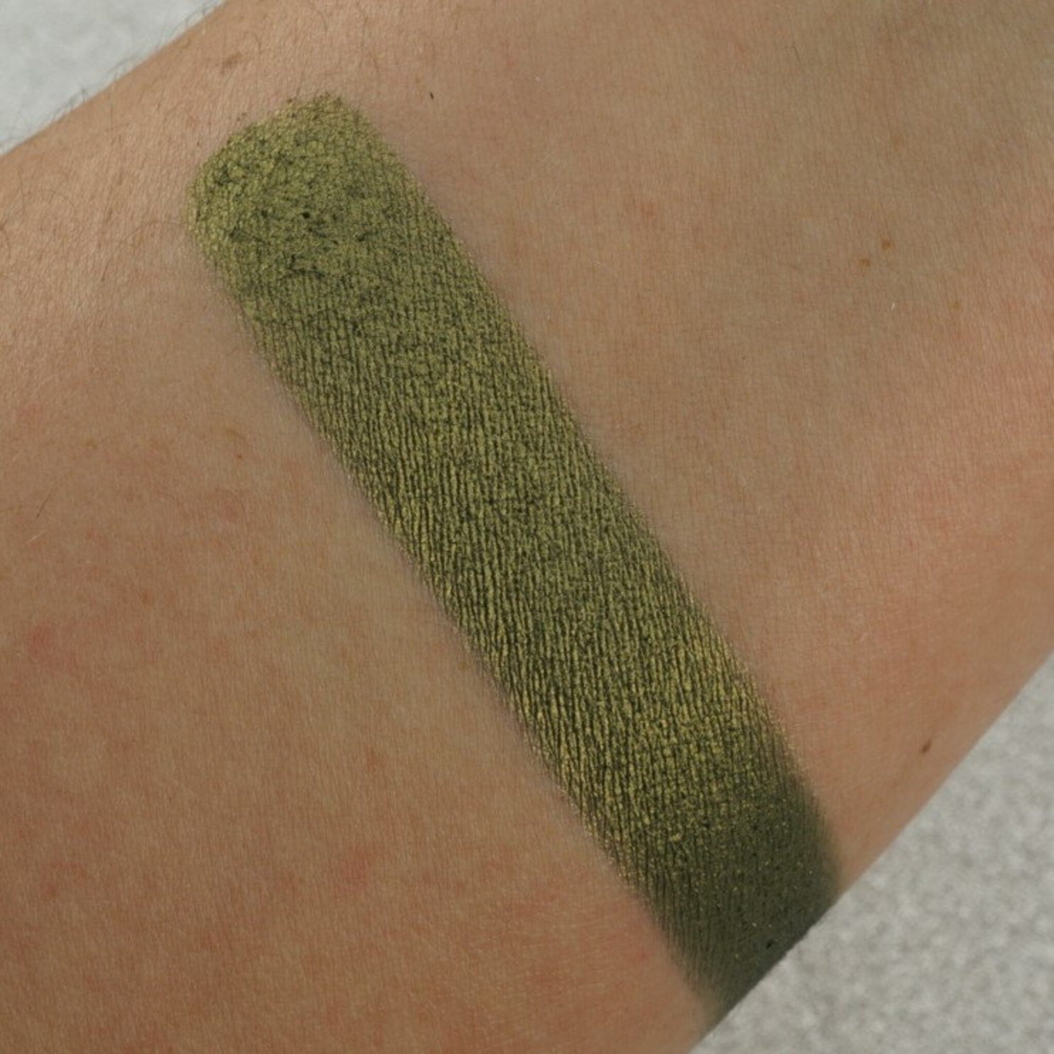 Close-up of pearlescent green eyeshadow pan with shimmer finish and smooth pressed pigment texture
