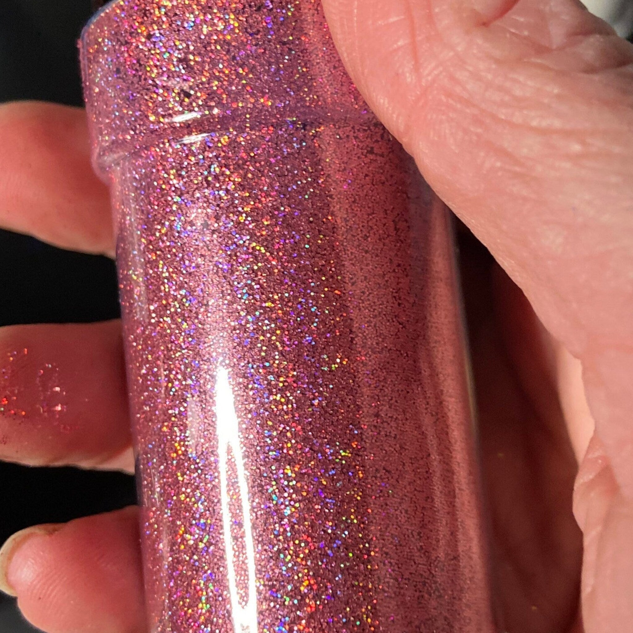 Hand applying holographic pink glitter eyeshadow to eyelid with fingertip, showcasing shimmering pigment blend