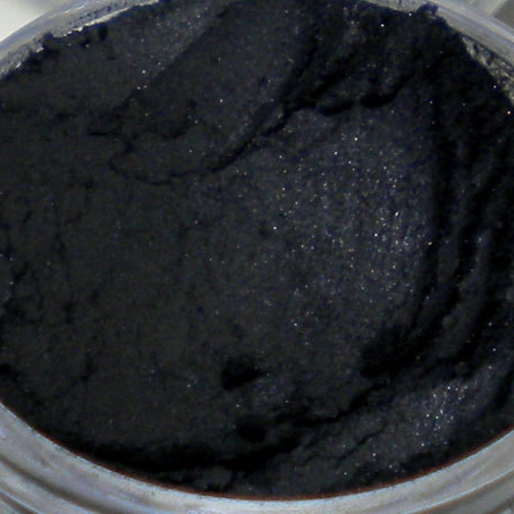 Black powder with textured surface and visible shimmer in container