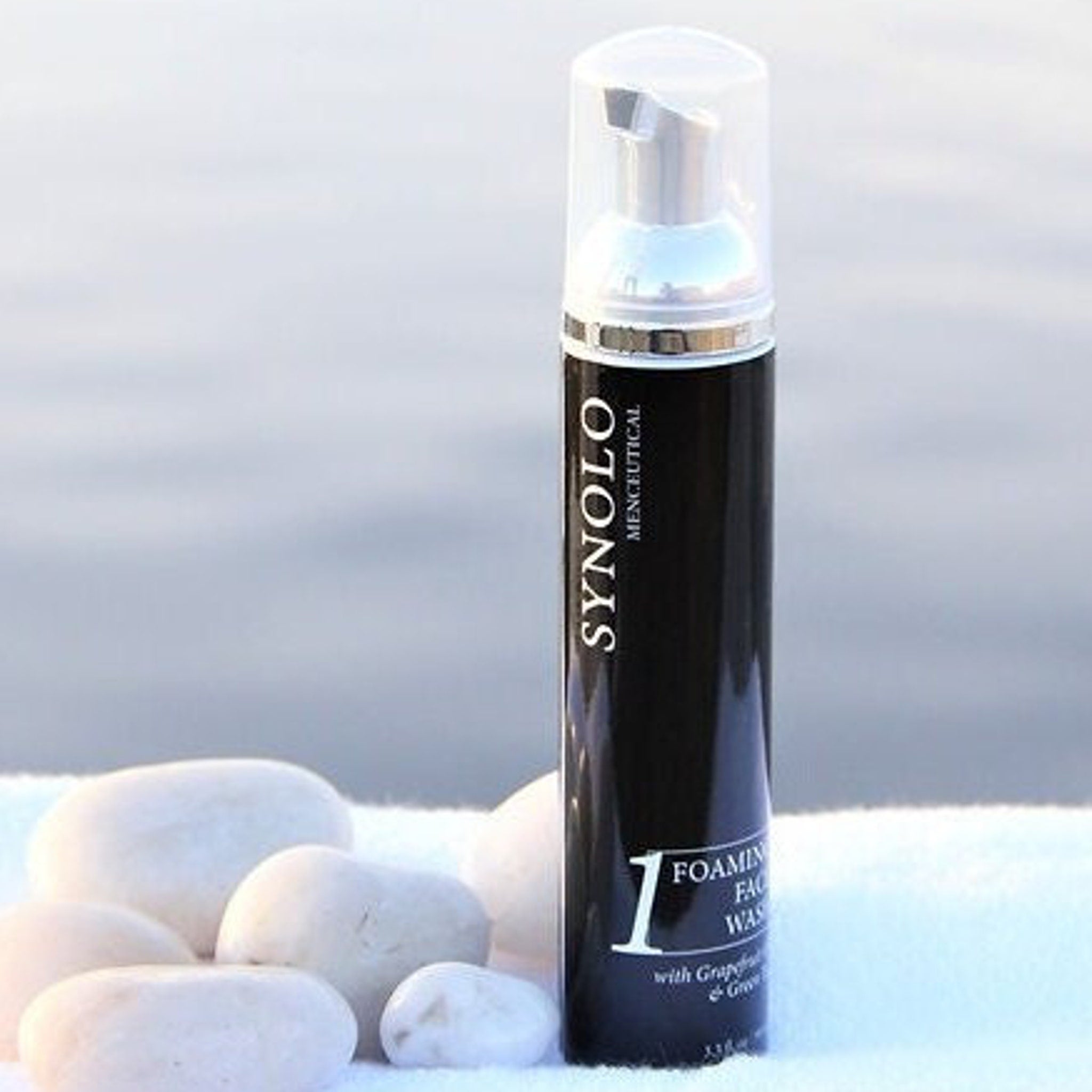 Foaming face wash bottle, black and silver, with white text, next to white stones