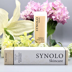Exfoliator Citrus Scrub, white and tan box with SYNOLO Skincare branding, floral background