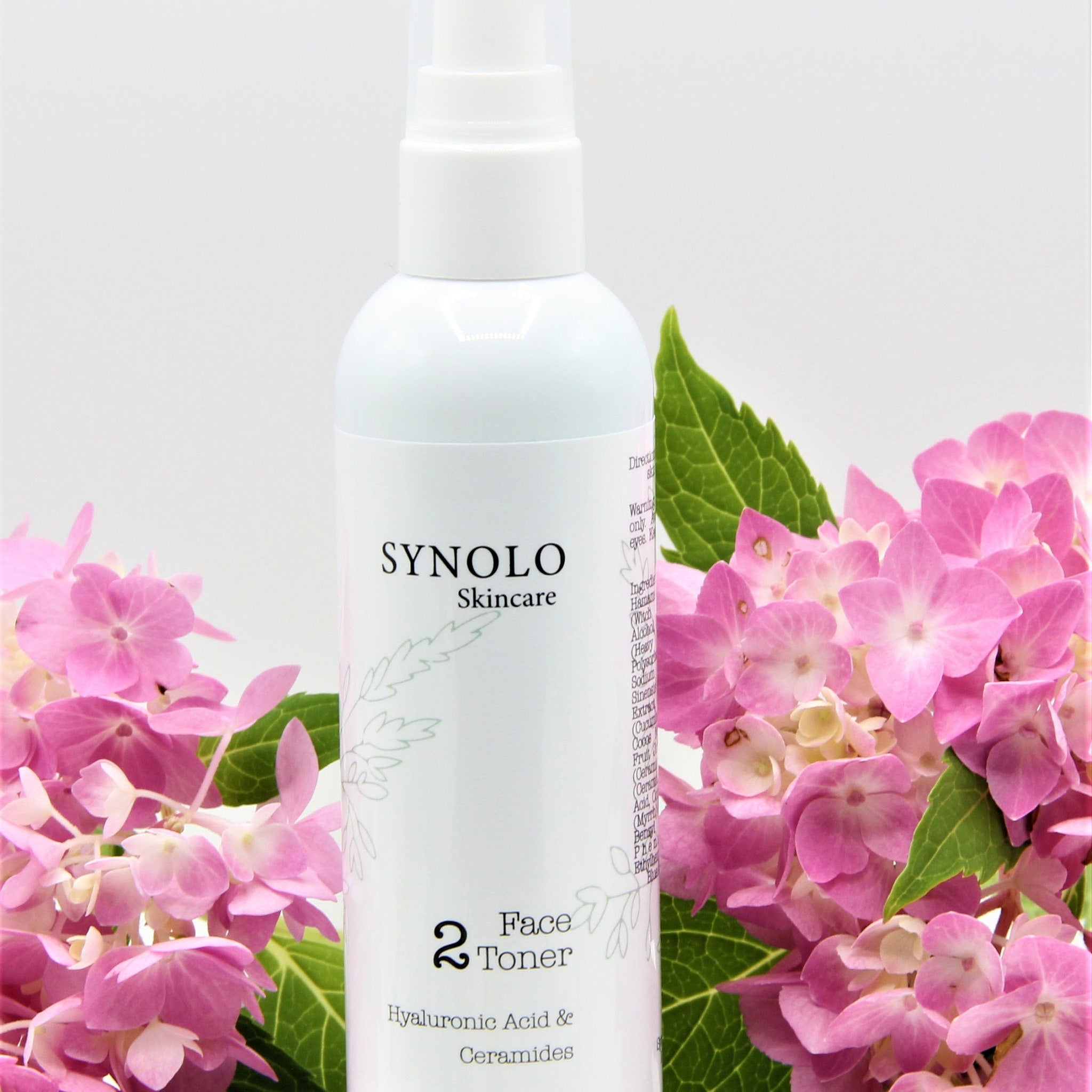 Face toner bottle, white plastic, pink floral background, Synolo Skincare label visible