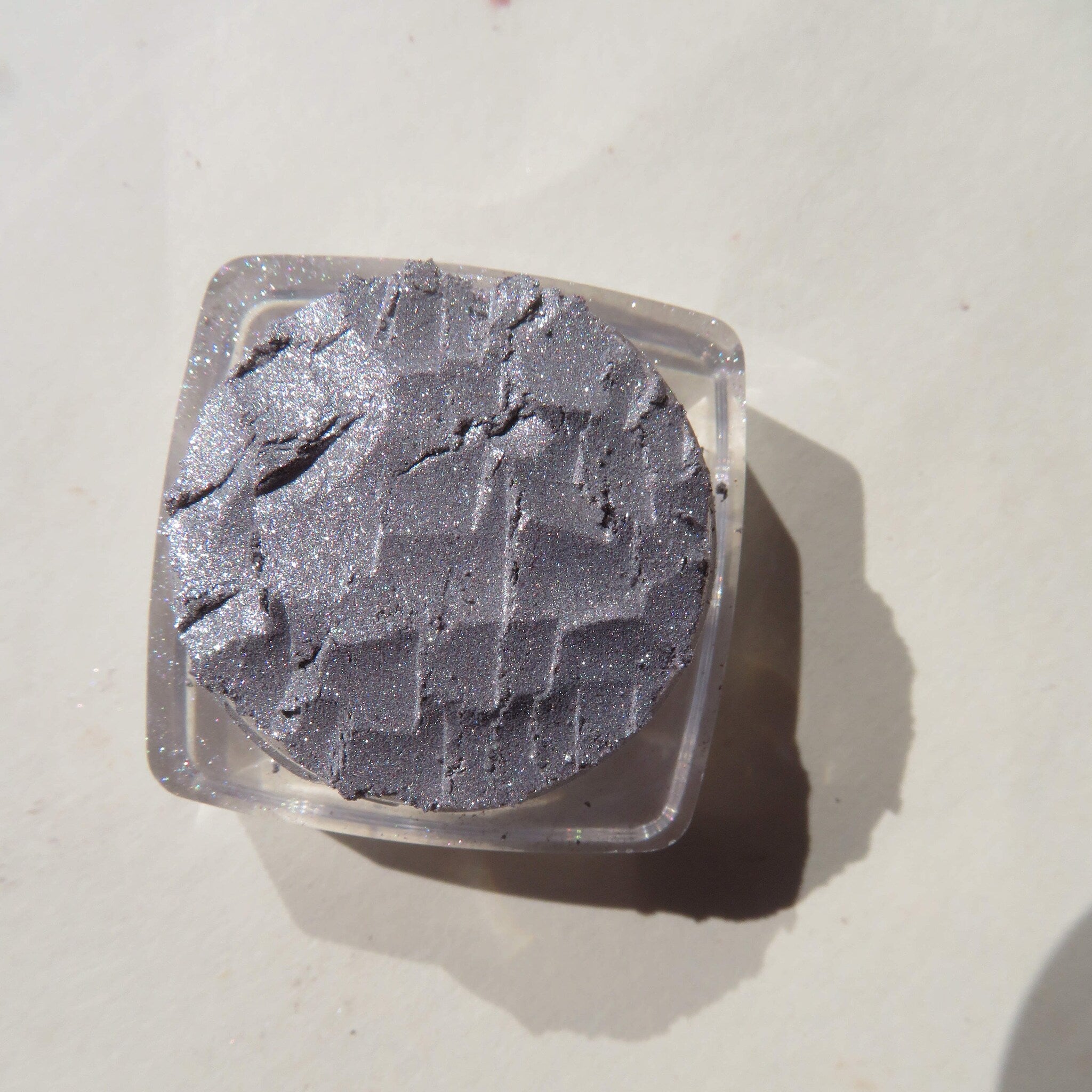Silver chrome loose pigment eyeshadow in clear jar with black screw-top lid on marble surface