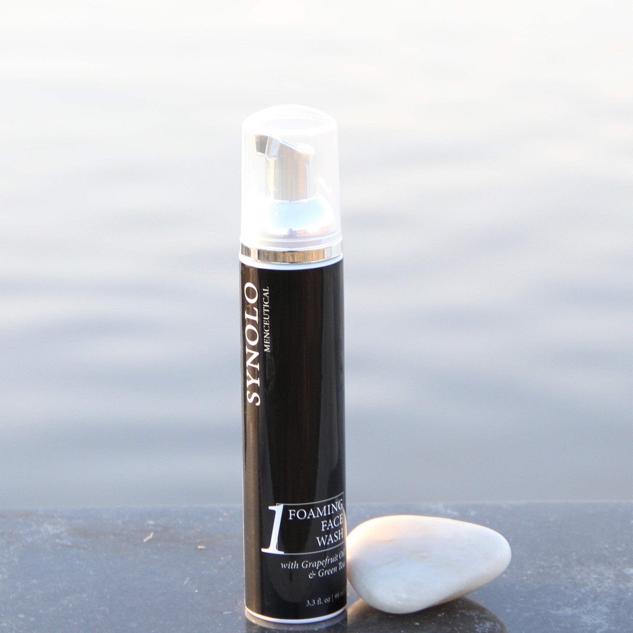 Foaming face wash black and silver bottle with white text and a white stone next to it