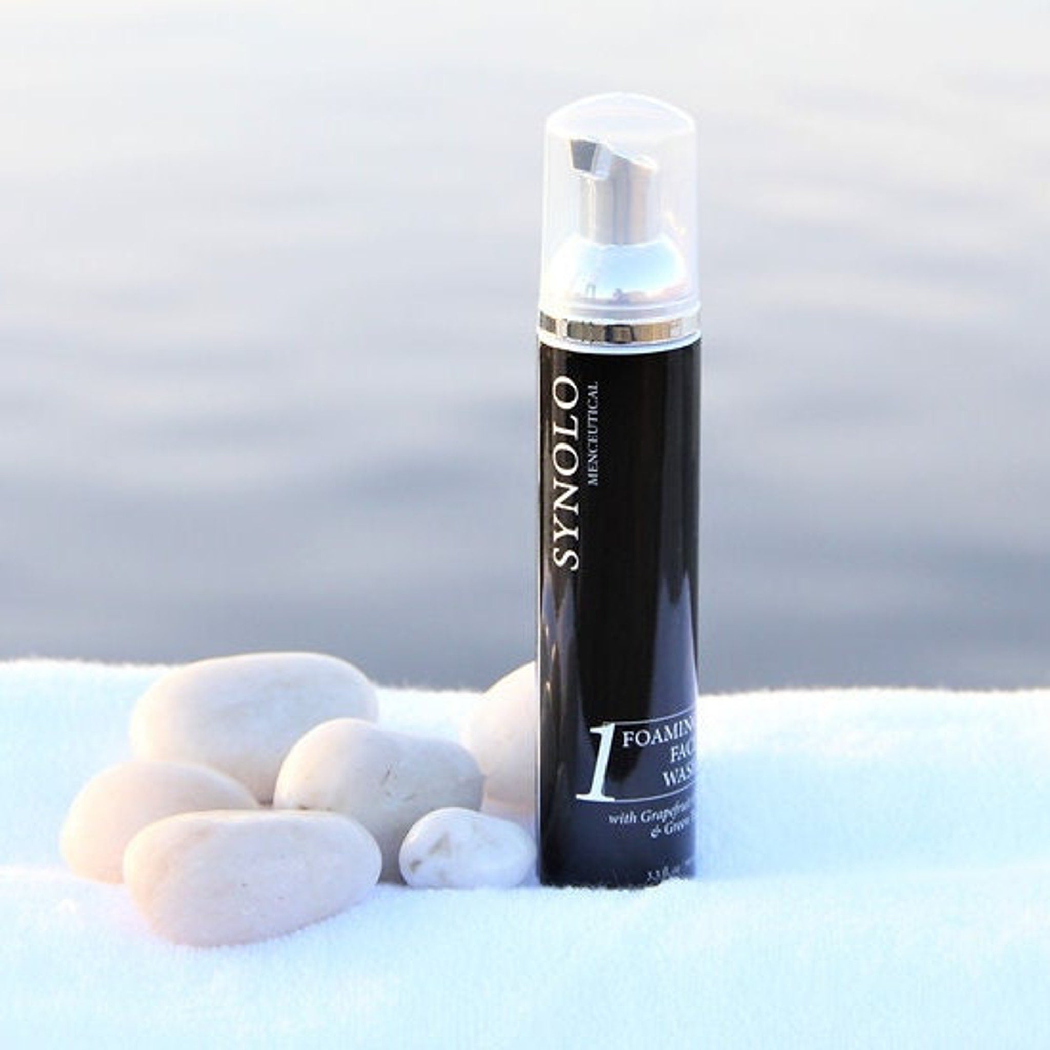 Foaming face wash bottle, black and silver, with "SYNOLO" branding and white text on a white towel