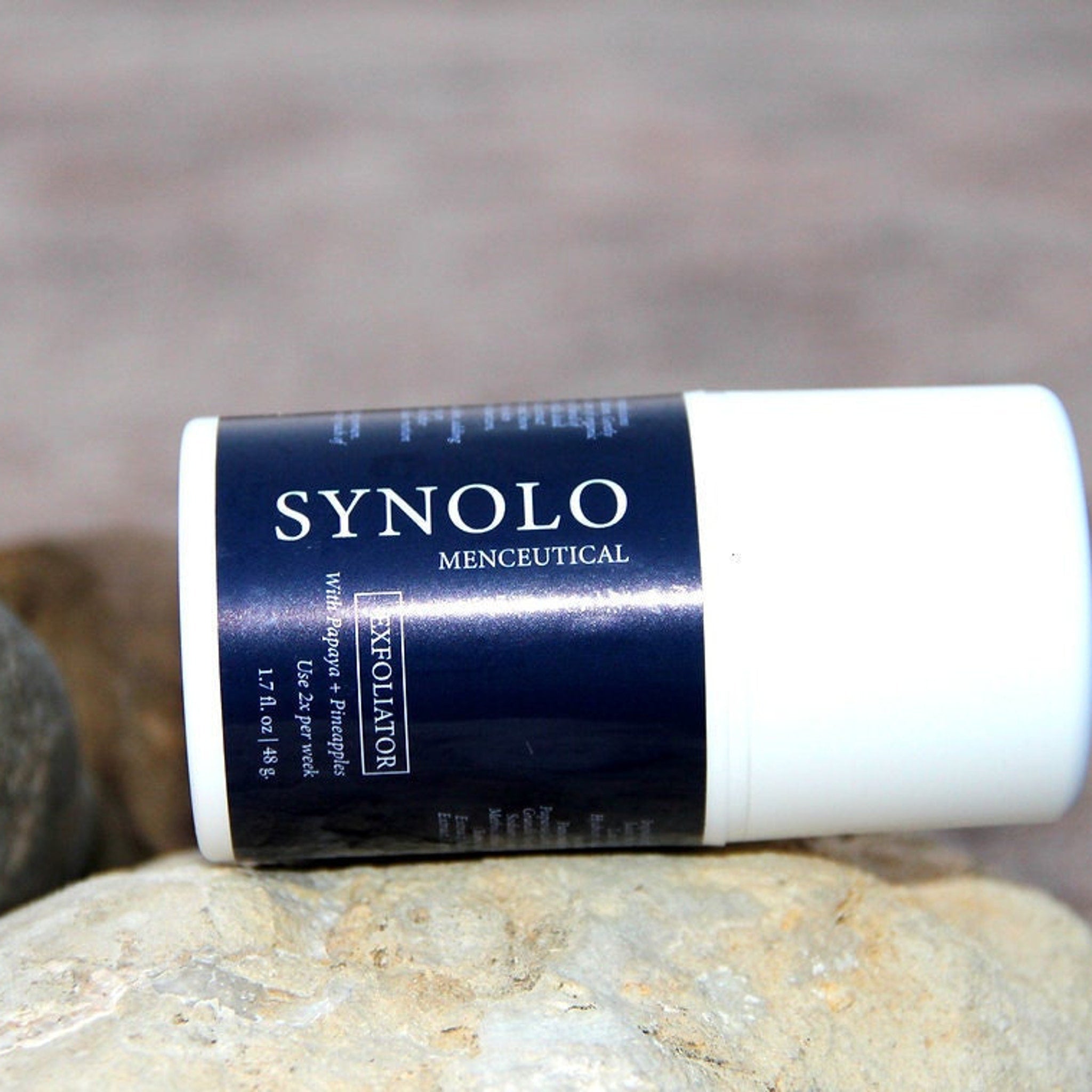 Exfoliator tube with white and navy blue label, SYNOLO brand displayed on rock surface