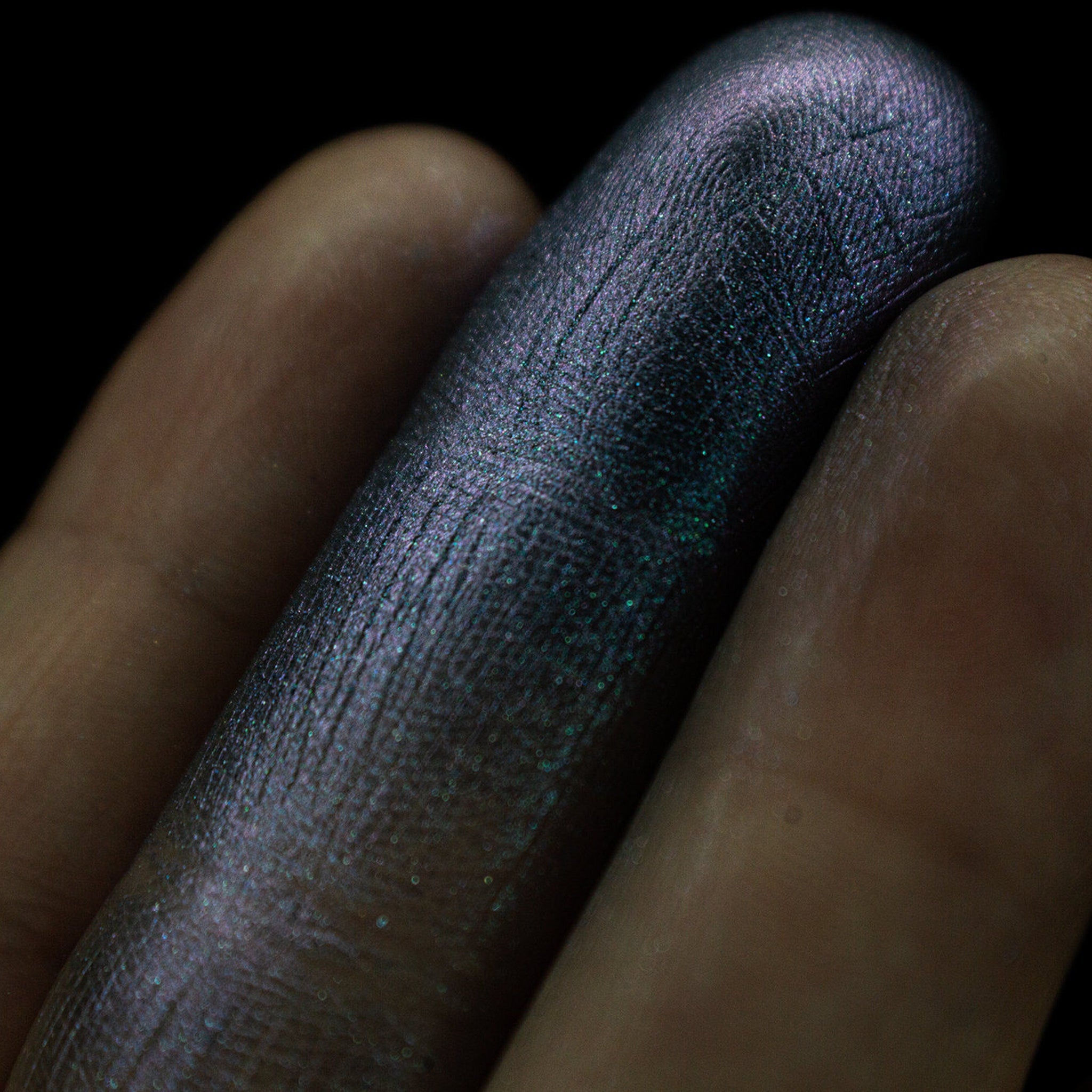 Hand applying grungy blue to purple duochrome eyeshadow with fingertip, showing shimmer transition