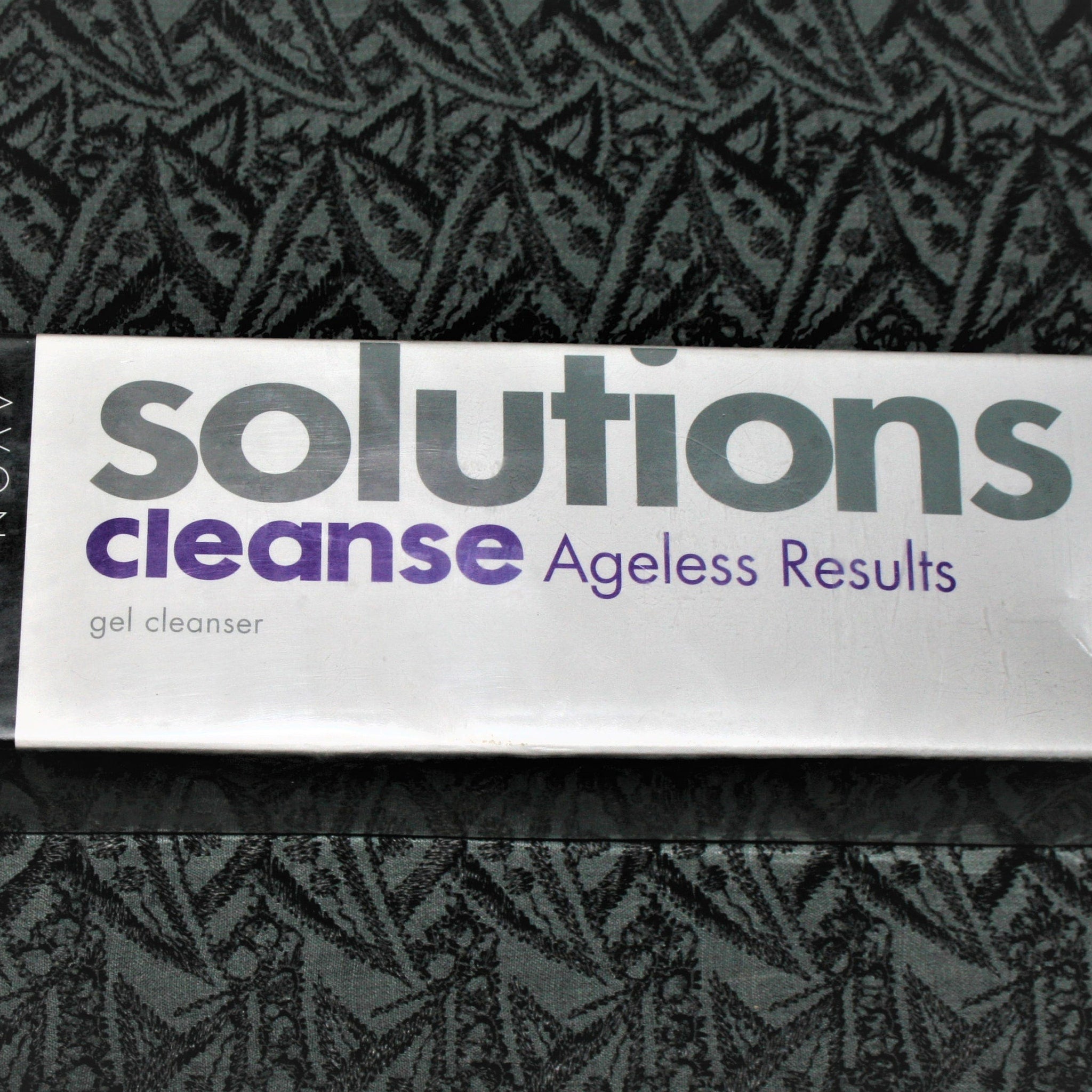 Facial cleanser product with white packaging, purple text, and Avon Solutions brand name visible