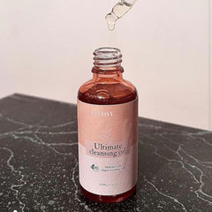 Cleansing oil bottle with pink label, clear liquid, and dropper, on black marble surface.