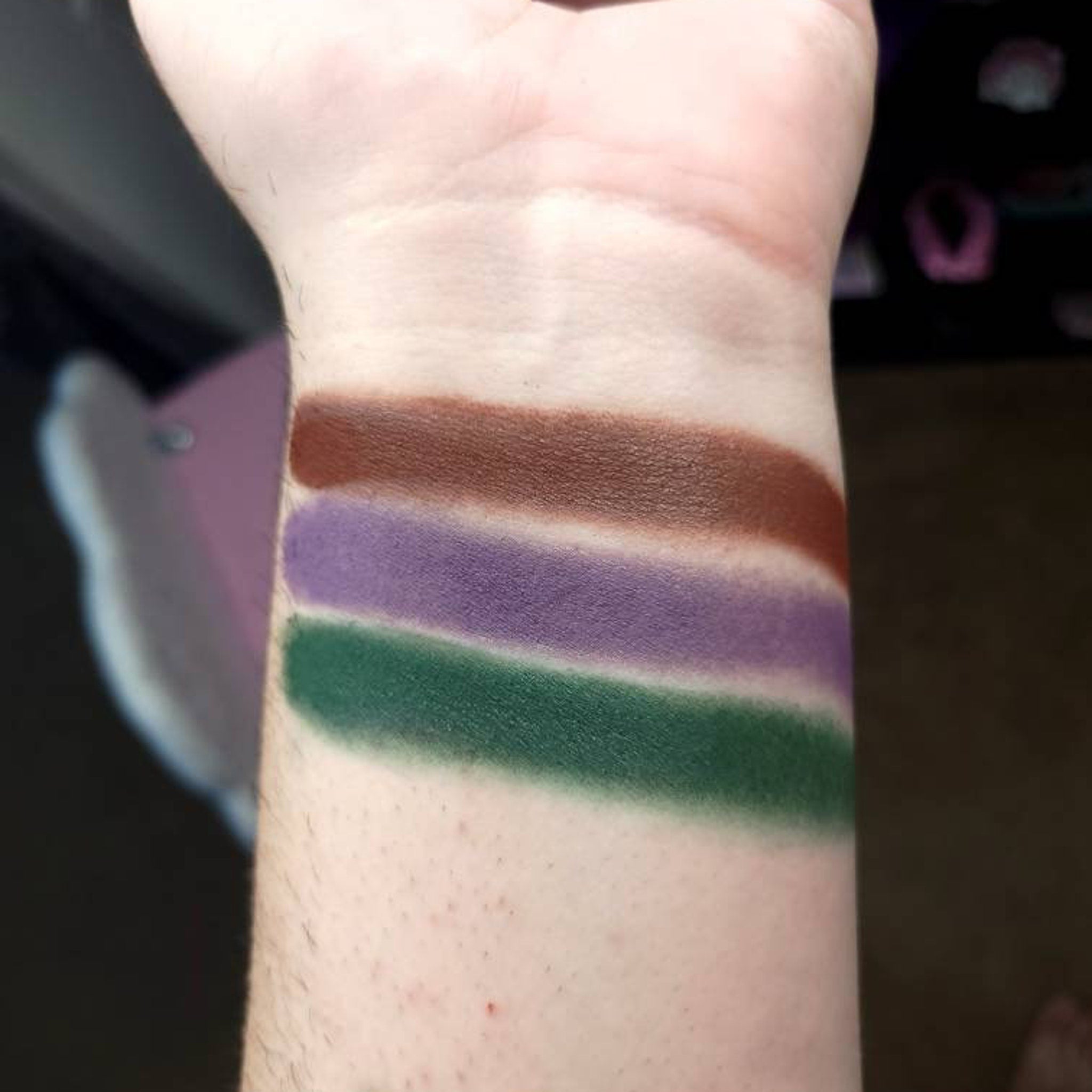Eyeshadow swatches on wrist, brown, purple, and green shades, applied on skin