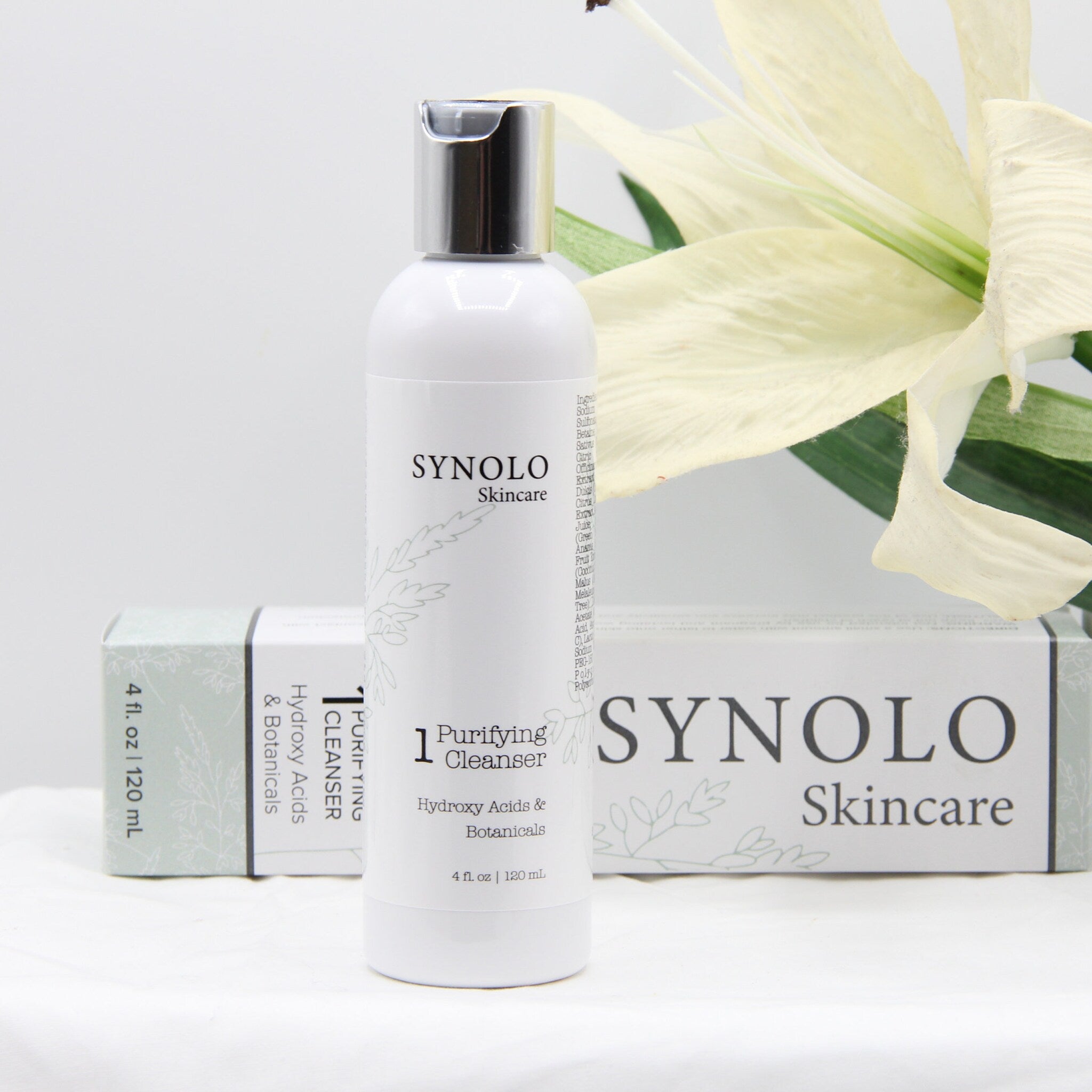 Purifying cleanser bottle with white and silver cap, Synolo Skincare branding, and floral design on packaging