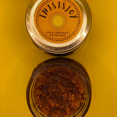 Skincare jar with brown granules, gold lid, and "THIS IS JOY" label on yellow background