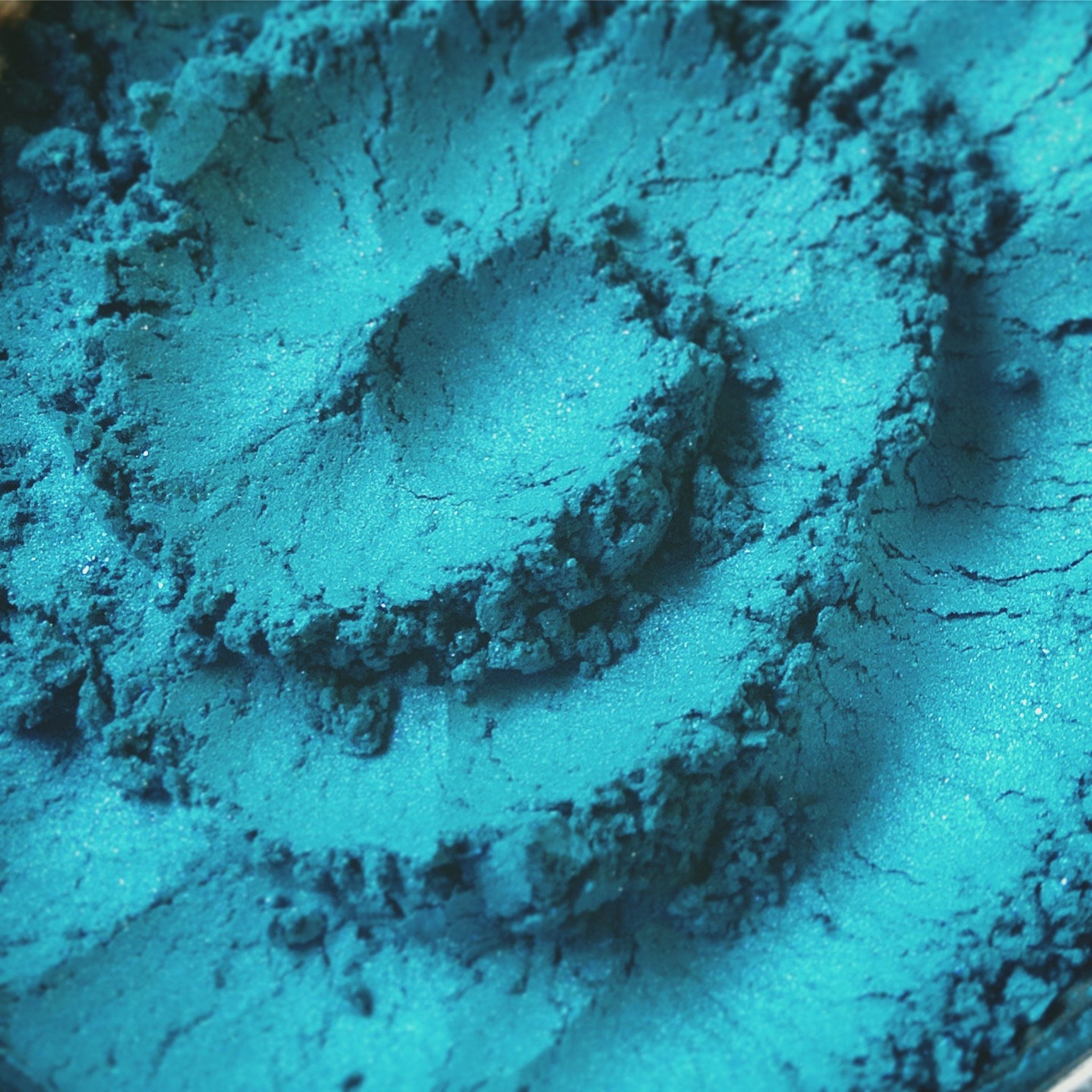 Side view of loose turquoise blue eye shadow with teal, iridescent aqua, and purple shimmer in mineral pigment jar