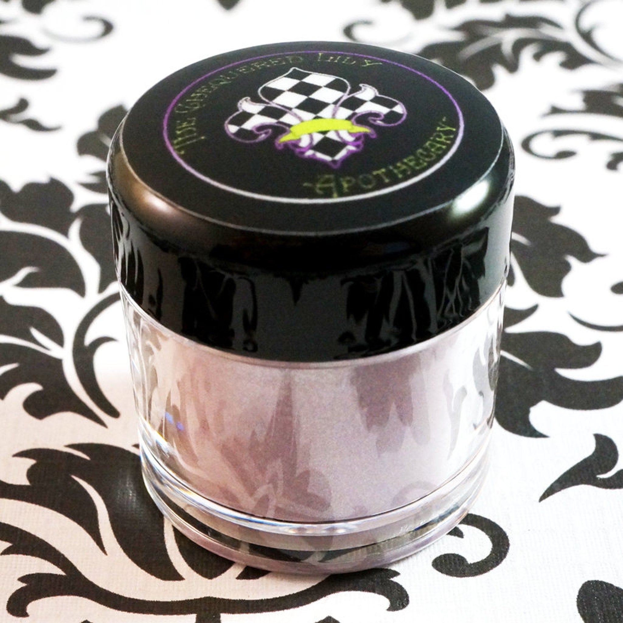 Jar with black lid, clear glass, and "The Unbequeathed Lily Apothecary" text on top