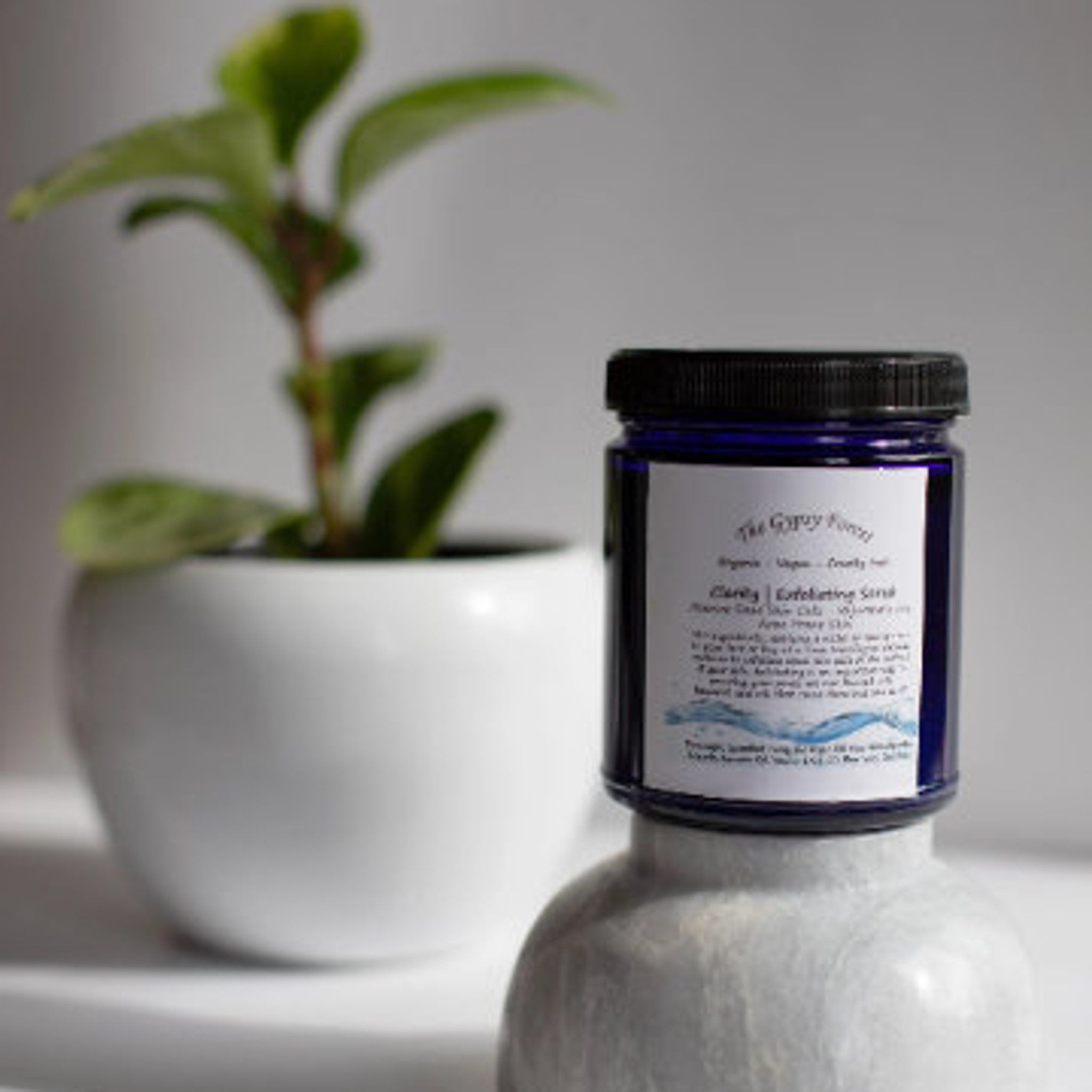 Exfoliating scrub jar with blue glass, black lid, and white label, "The Gypsy Forest" brand