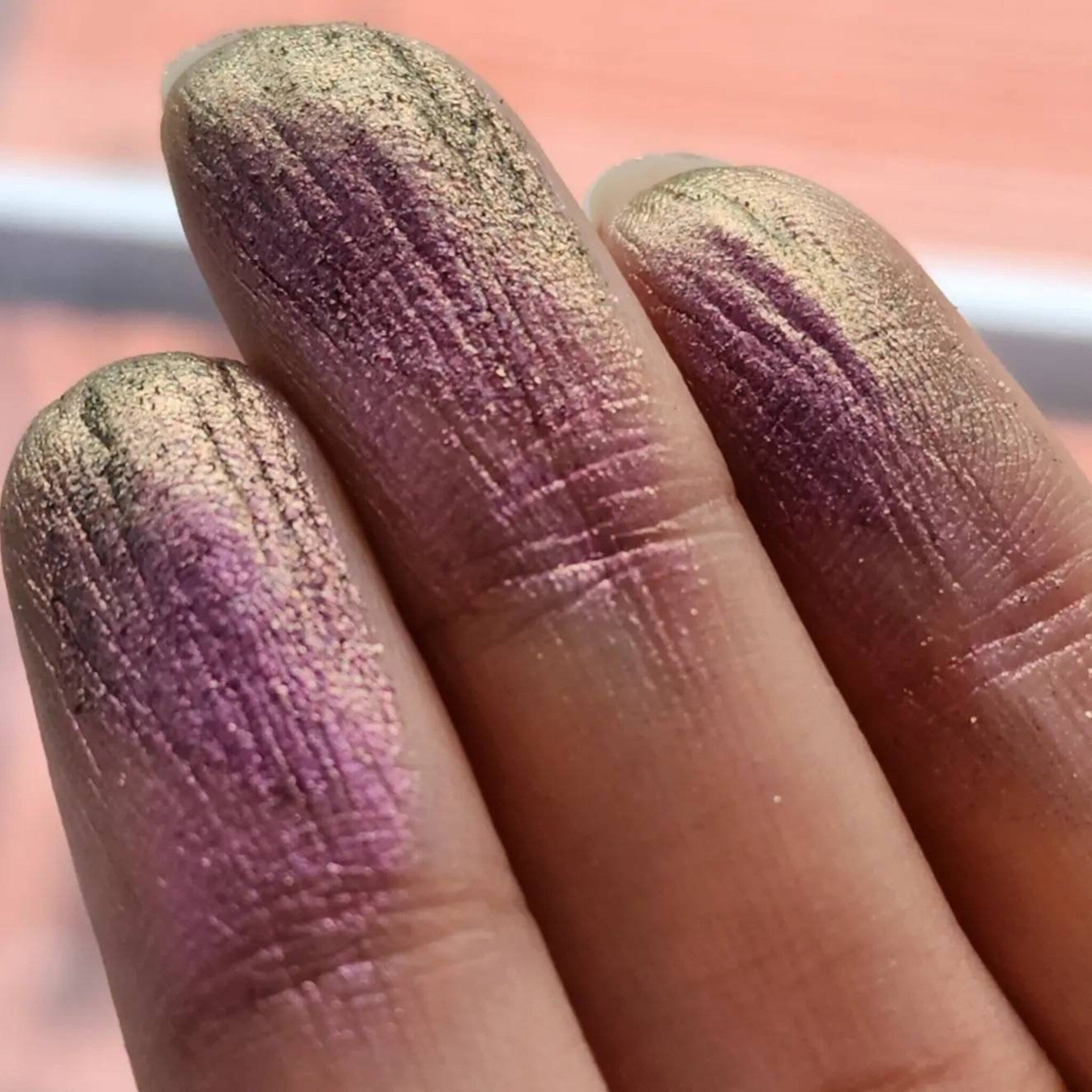 Close-up of fingers applying purple-olive shimmer eyeshadow with color-shifting sparkle to eyelid