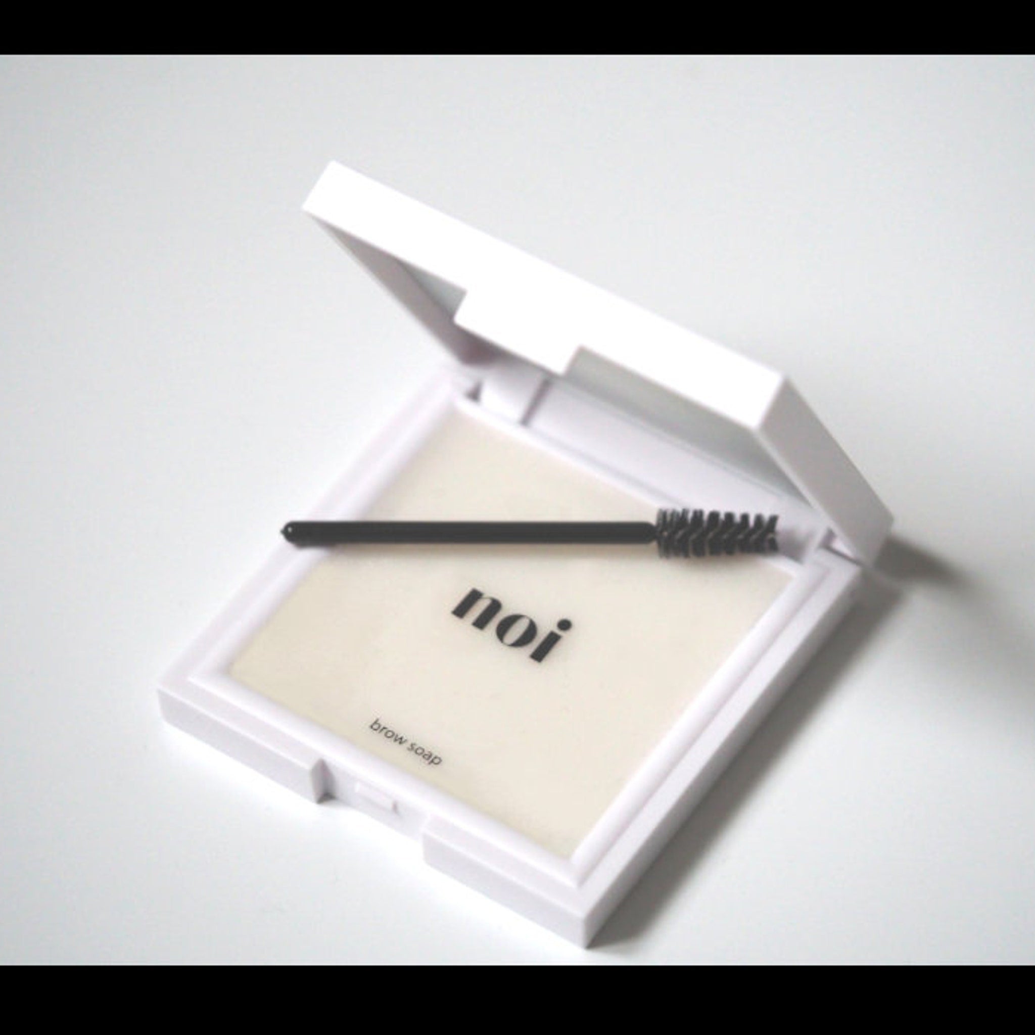 Brow soap in white compact with black applicator, "noi" text visible
