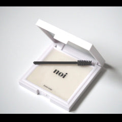 Brow soap in white compact with black applicator, "noi" text visible