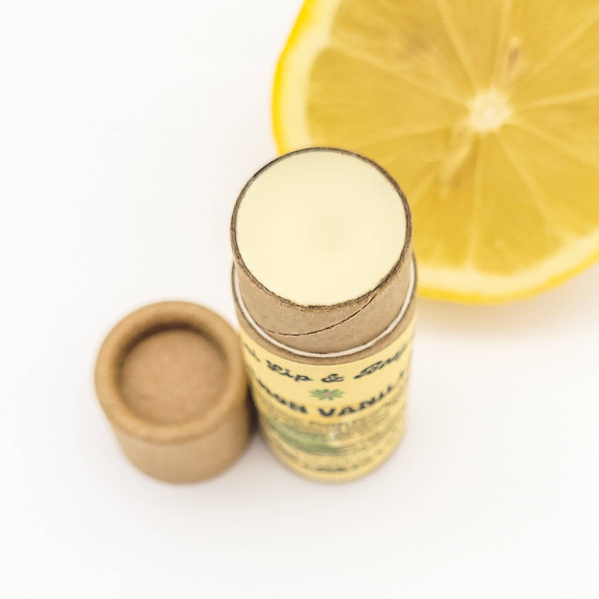 Lip balm tube with yellow balm, brown cardboard tube, and lemon slice on white background