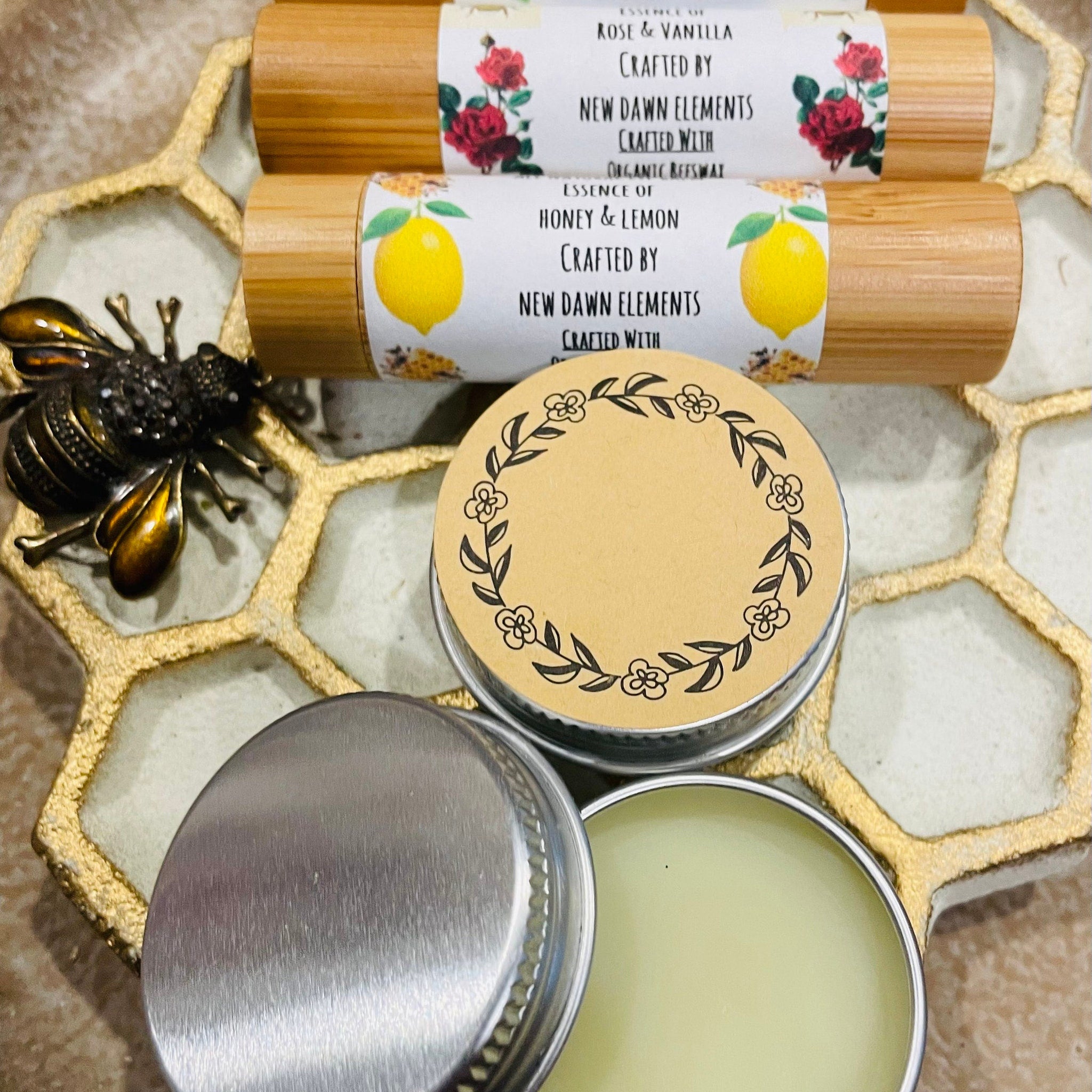 Lip balm tubes with bamboo casing, floral labels, and New Dawn Elements branding, with a lip balm tin on a decorative surface