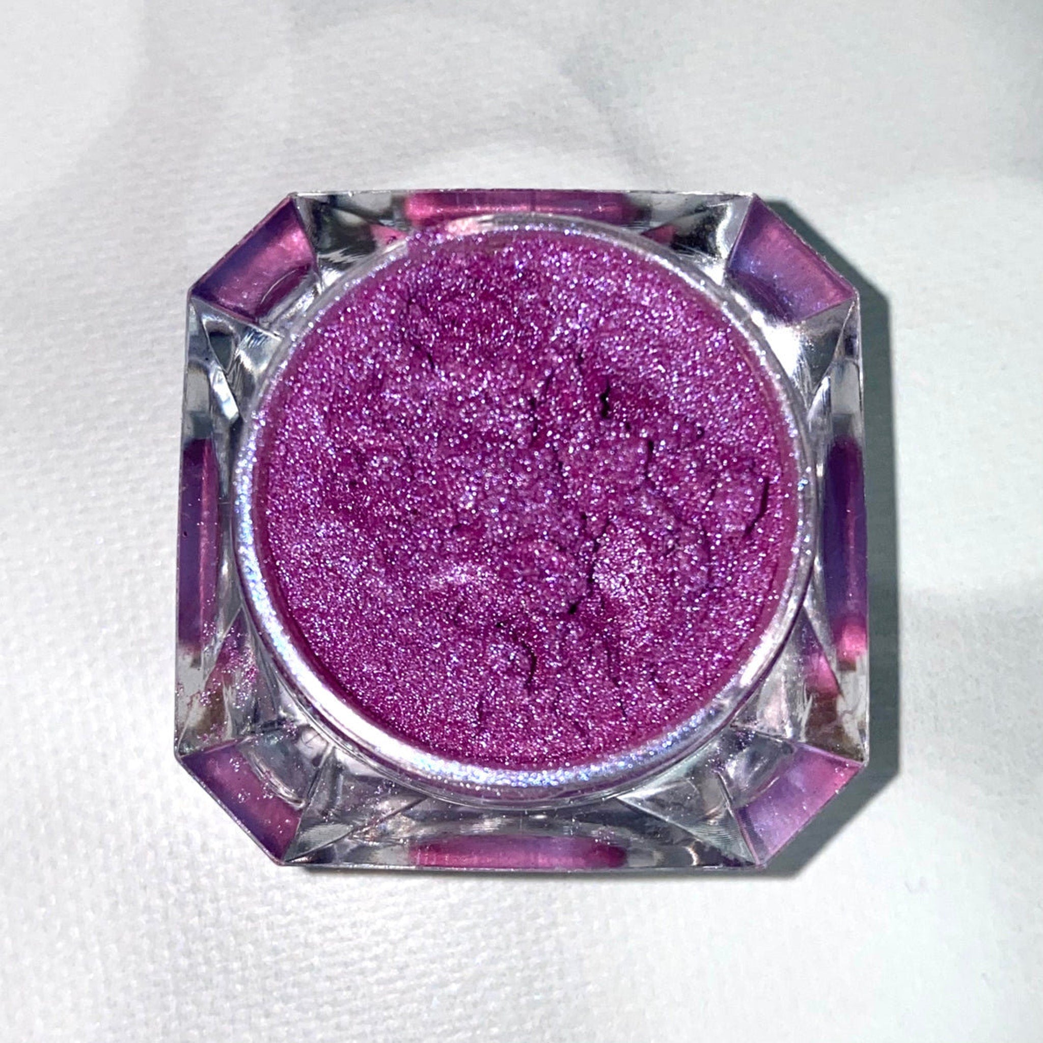 Close-up of fingertips applying shimmery purple and blue eyeshadow to eyelid with smooth blending motion