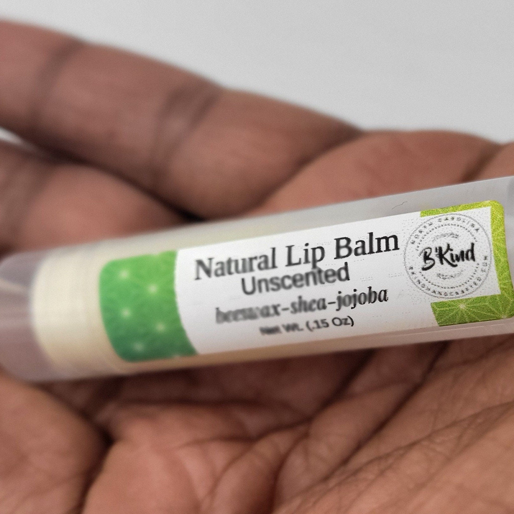 Lip balm tube with green patterned label, white text, and B'Kind brand name held in hand
