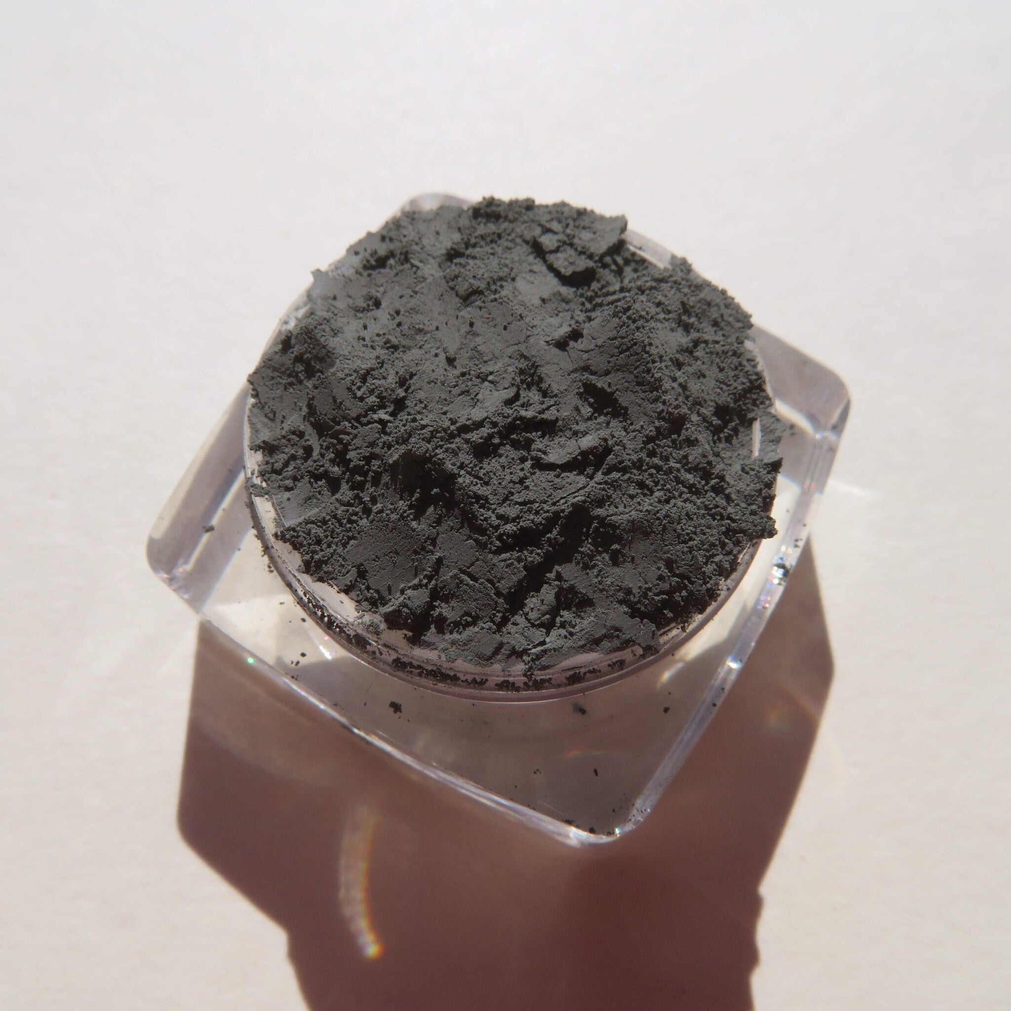 Close-up of loose dark matte green tea mineral eyeshadow powder with fine mica shimmer in a jar