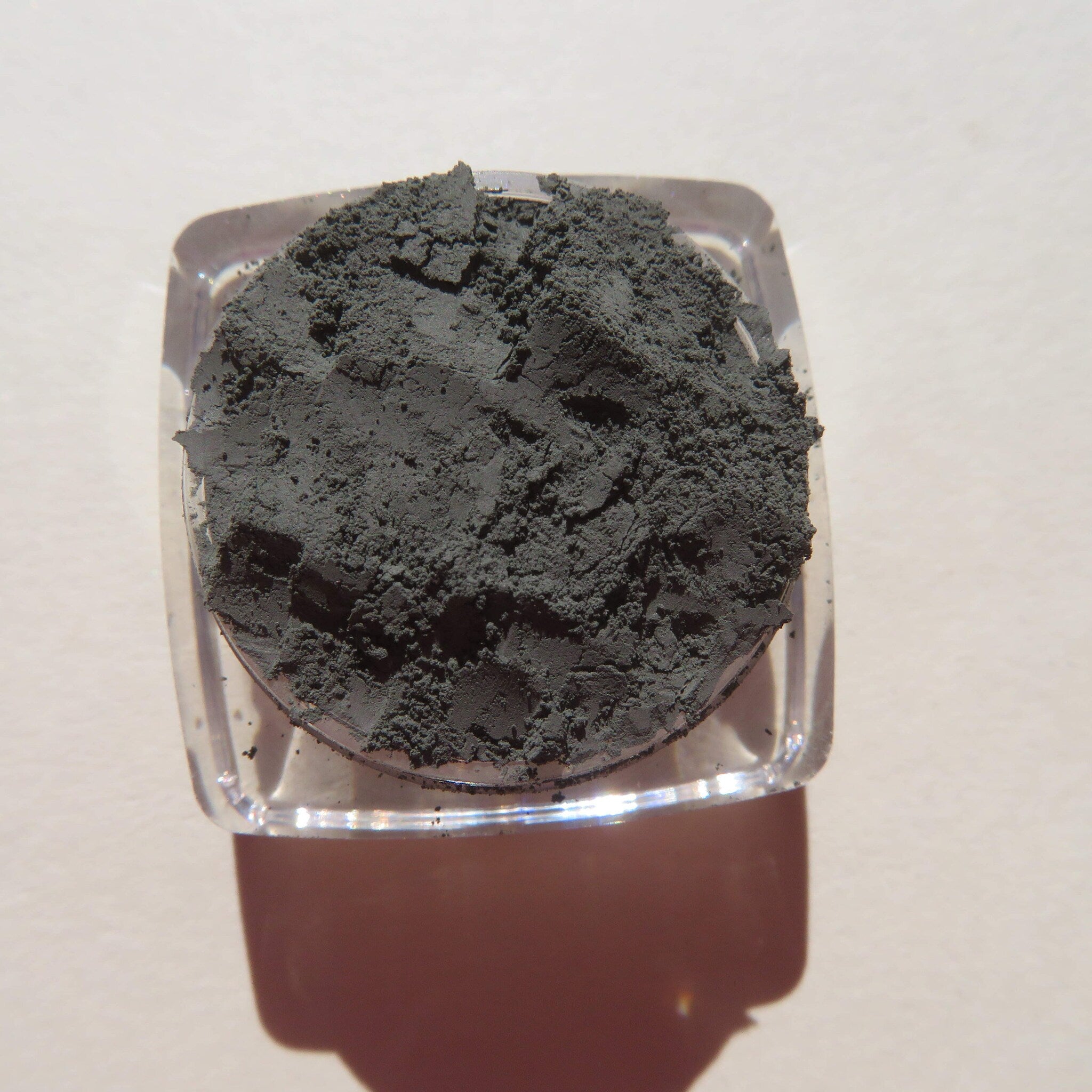 Hand applying dark matte green tea mineral eyeshadow with a fluffy brush, showcasing loose powder texture