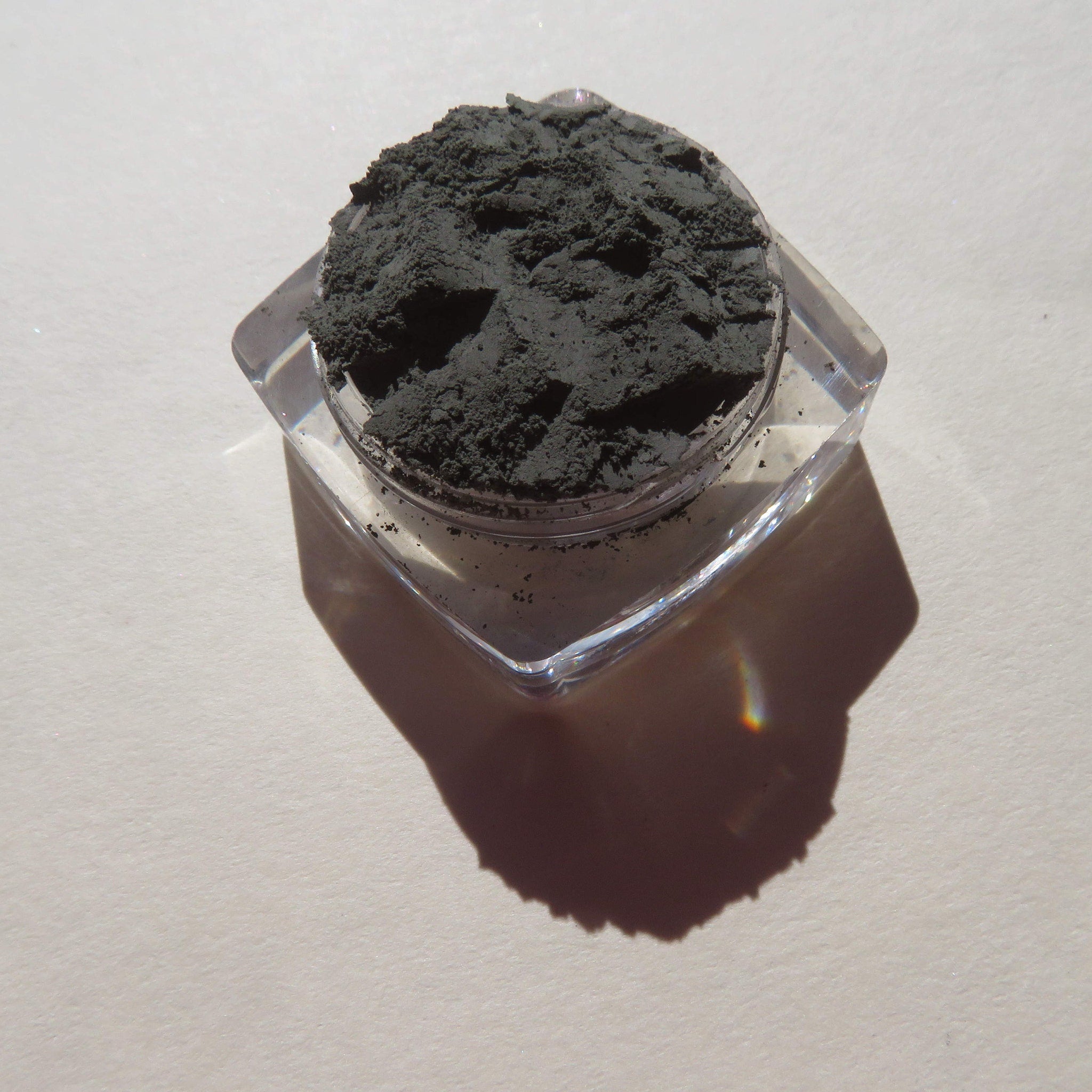 Side view of dark matte green tea mineral eyeshadow in loose powder form, showcasing rich pigment texture