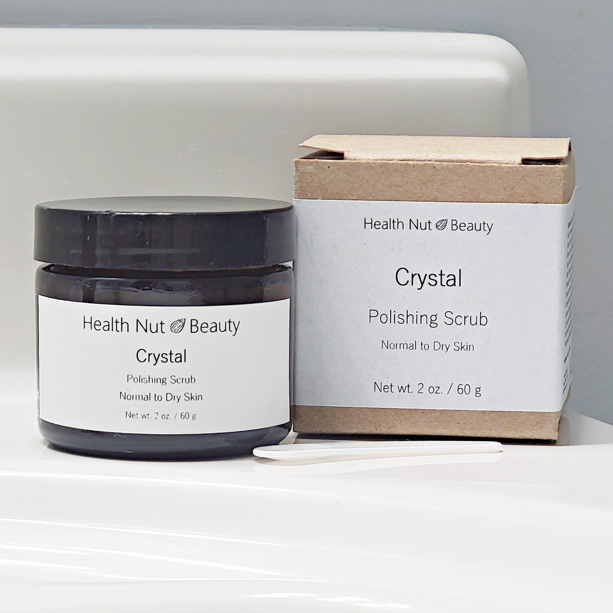 Polishing scrub jar with black lid and white label next to a brown box with white label, Health Nut Beauty brand