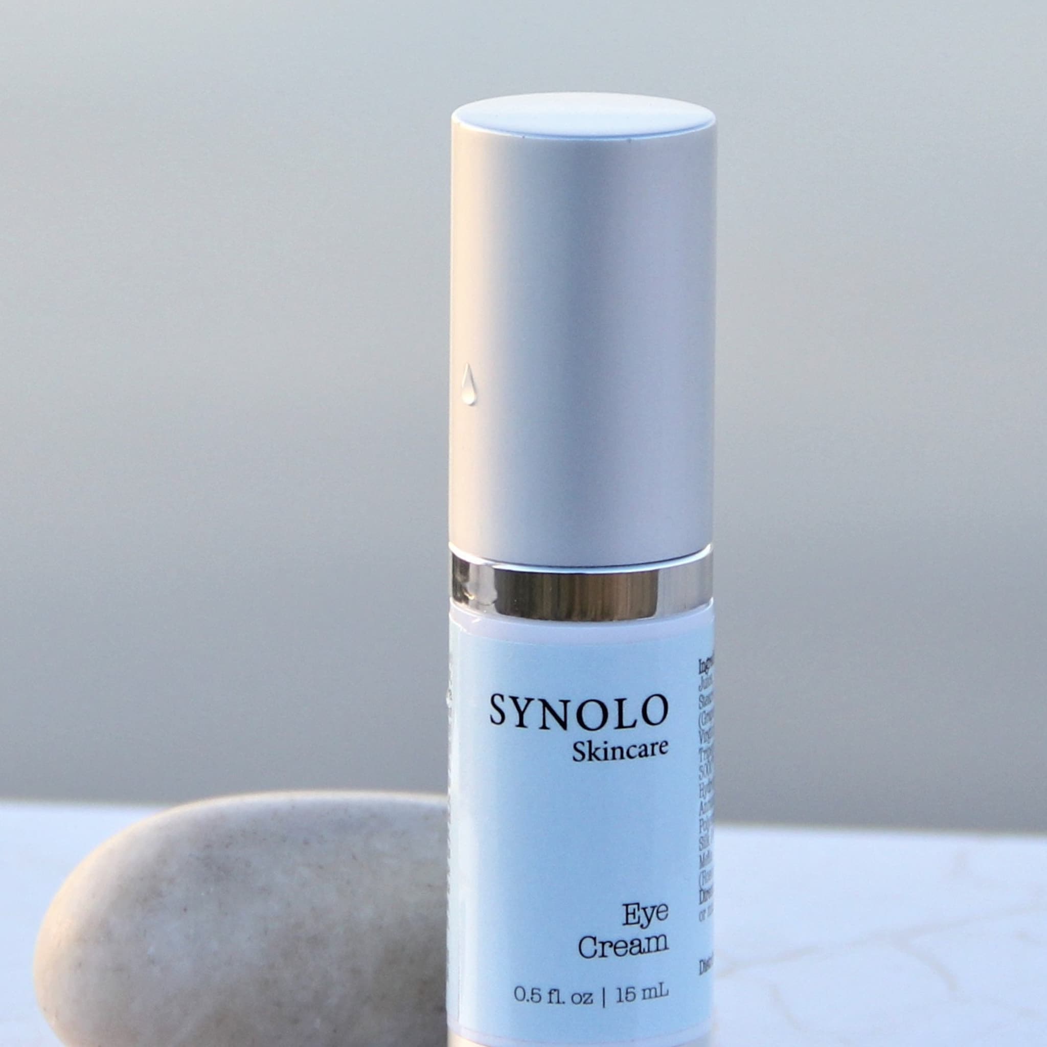Eye cream bottle, light blue and silver, with "SYNOLO Skincare" text visible on label