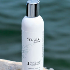 Purifying cleanser bottle, white with silver cap, Synolo Skincare branding, leaf design