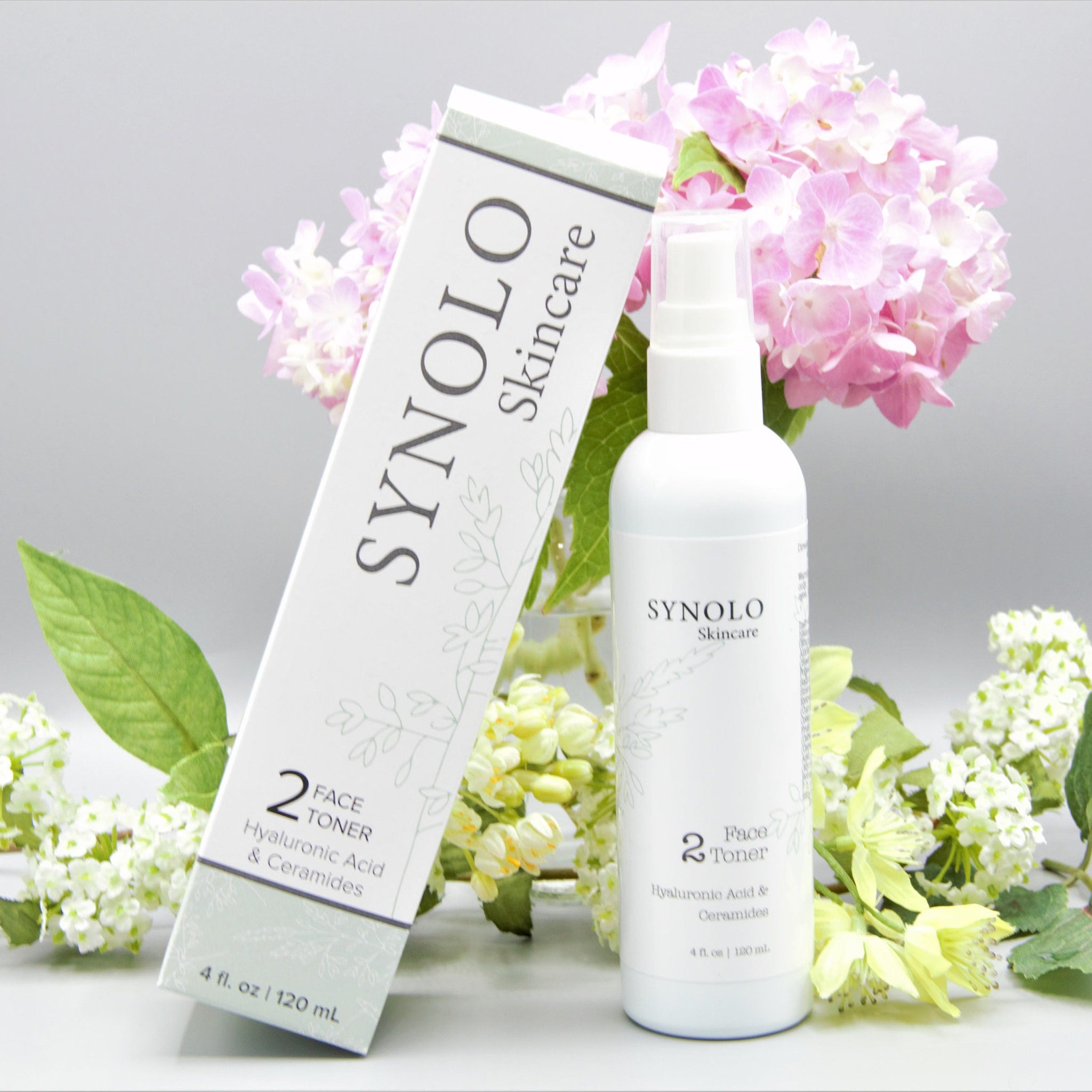 Face toner bottle and box with white and green text, white background, and flowers