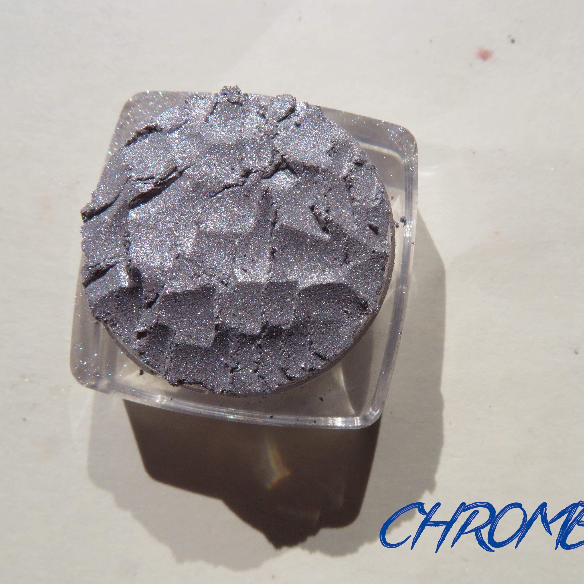 Side view of shimmery silver chrome loose pigment eyeshadow jar catching light at an angle